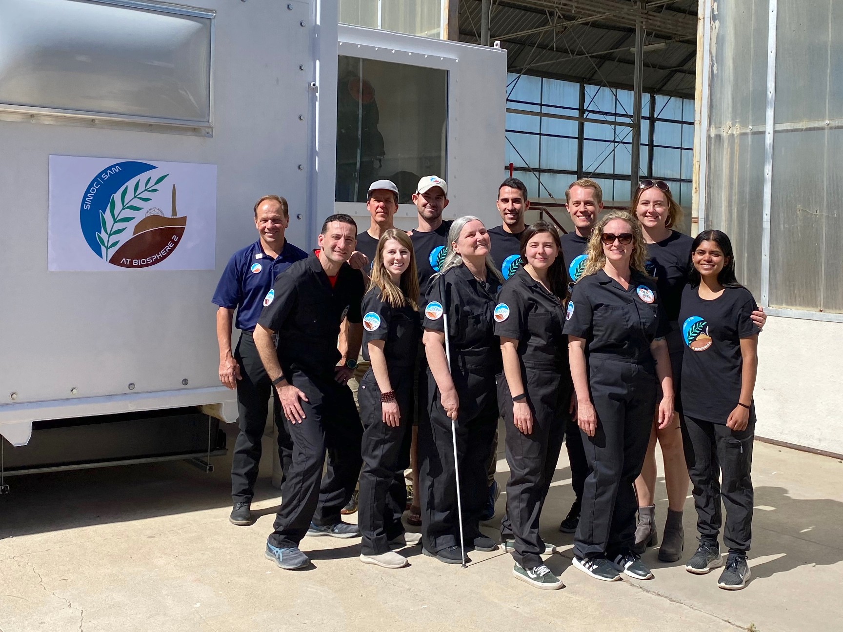 Twelve people making up the Inclusion I crew and some of the SAM team members stand in front of the Space Analog for the Moon and Mars module.