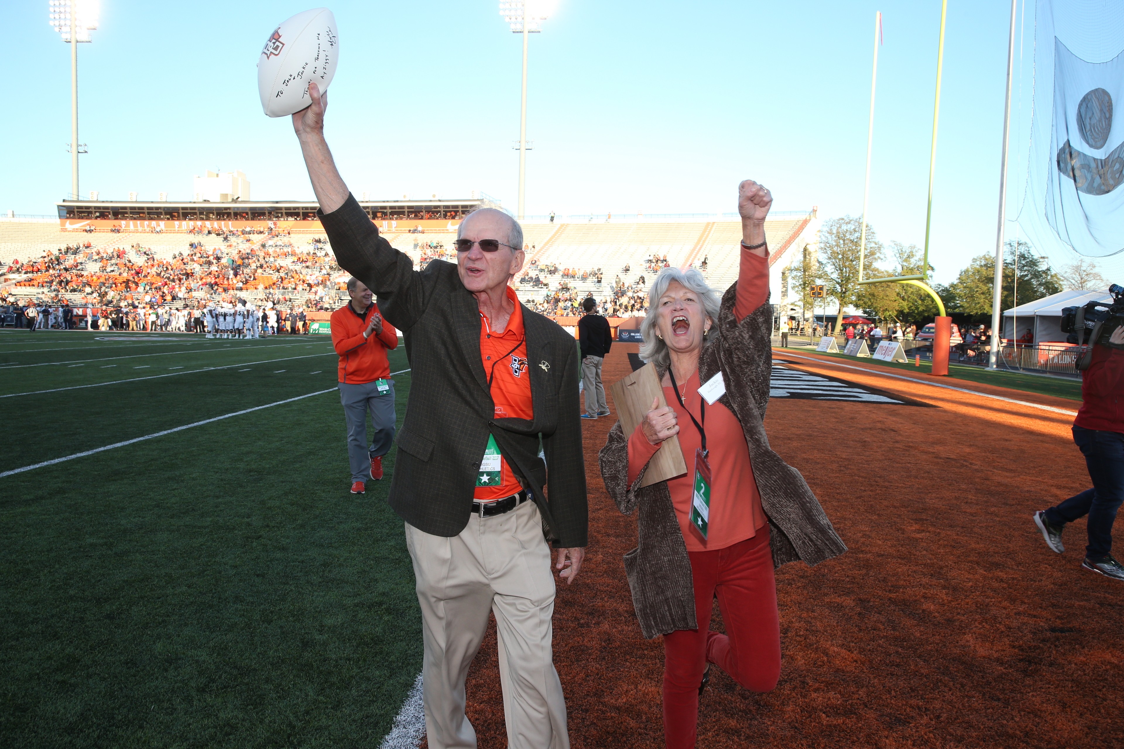BGSU alumni Jack and Jackie Harbaugh cheer and hold a football at Doyt L. Perry Stadium