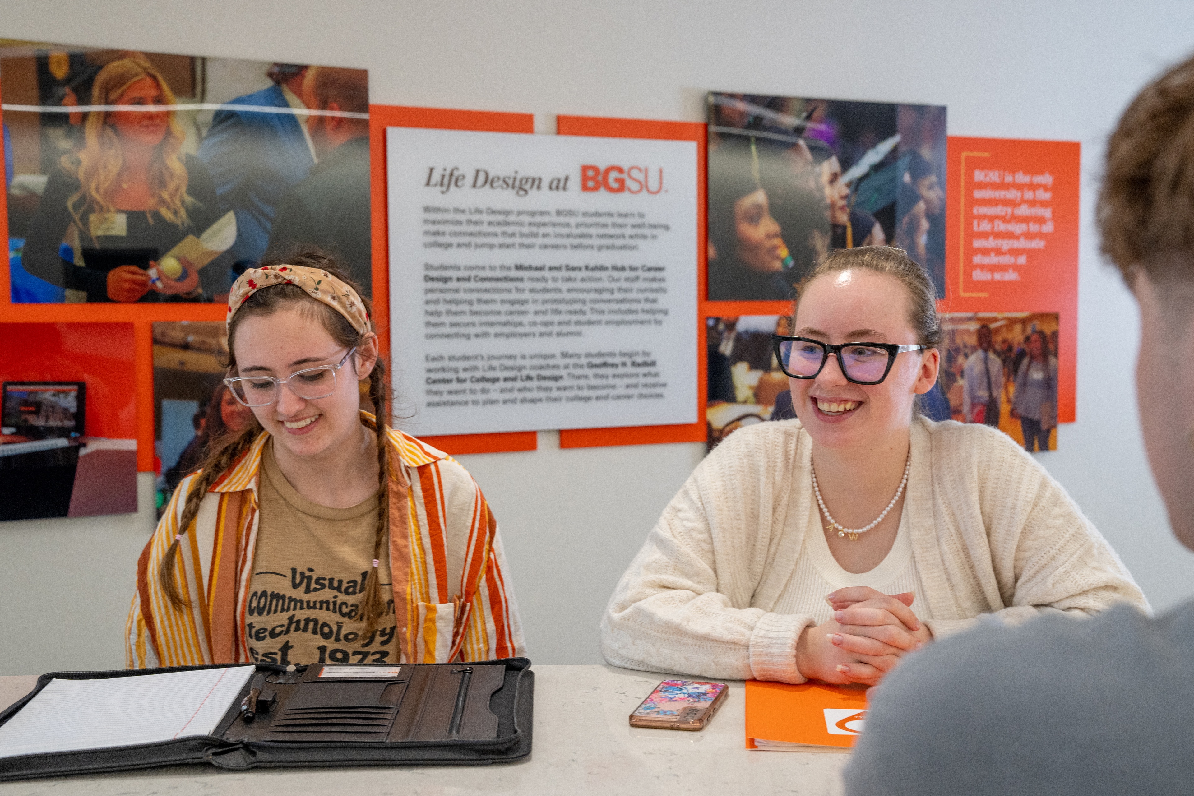 Two students smile while sitting at a table in the Kuhlin Hub.
