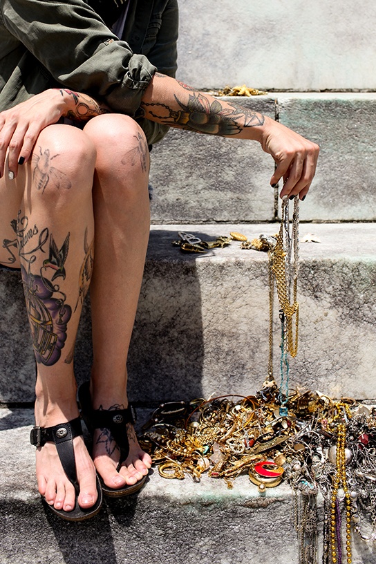 Close-up of a woman's leg with tattoos on it next to a pile of old jewelry on a step