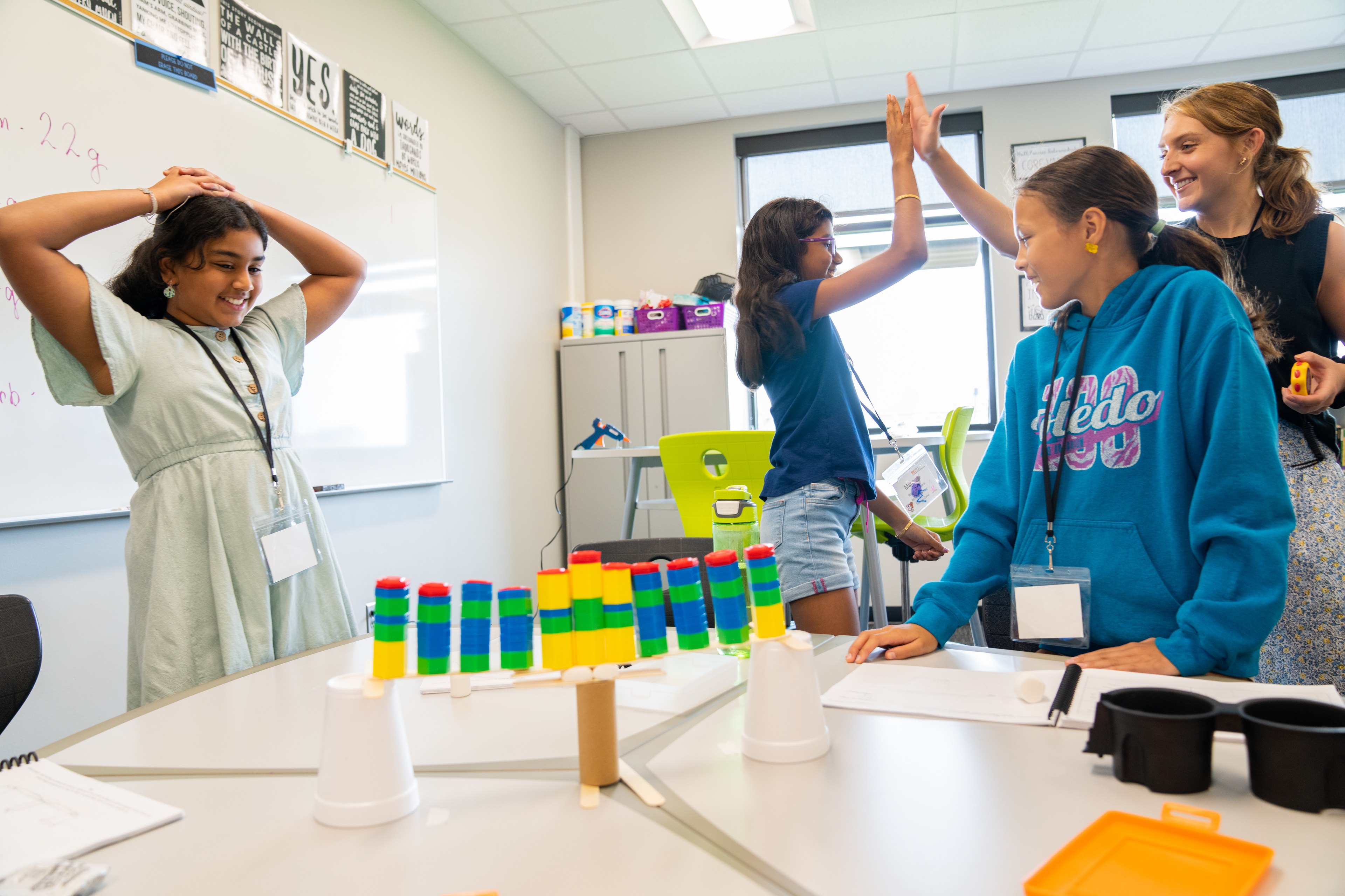 Tutor Jillian Filipiak high fives a student for completing a successful engineering project that used a toilet paper tube and two styrofoam cups to make a bridge. 