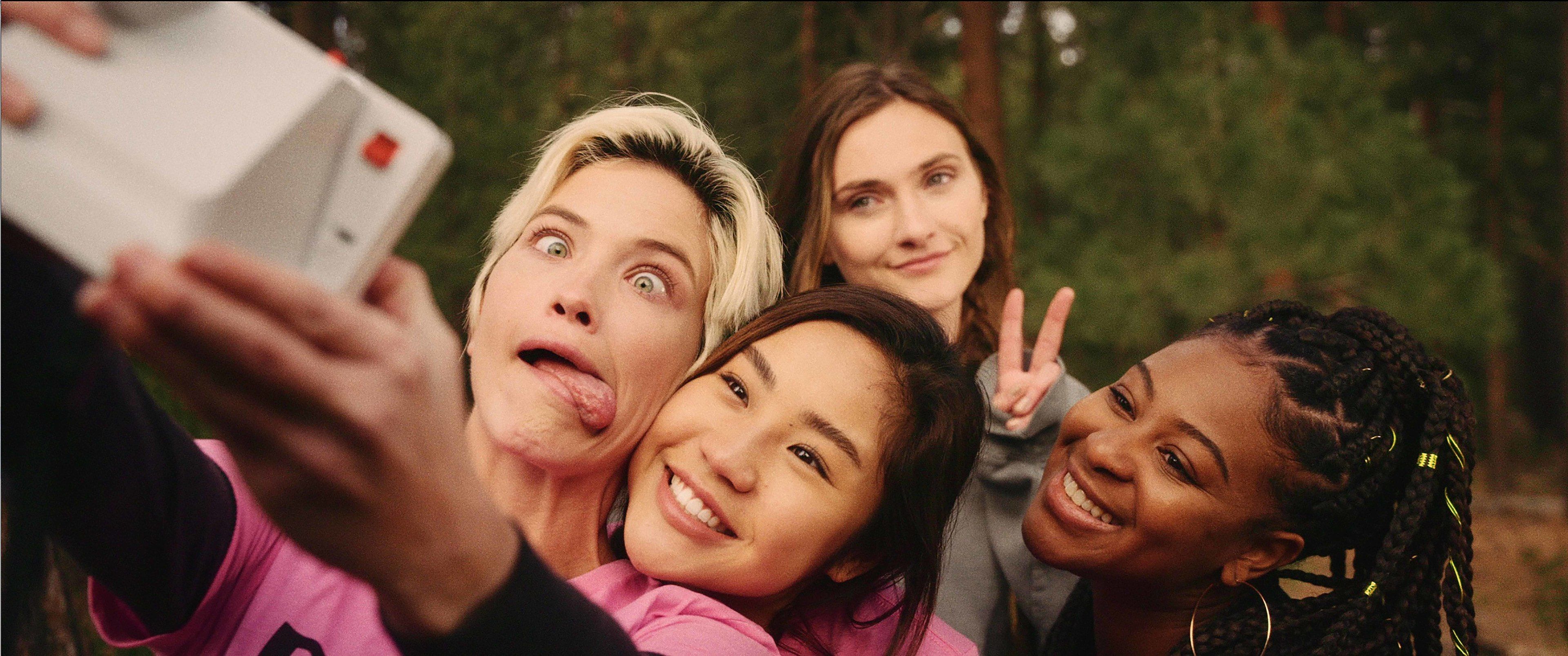 Four women smile at the camera while taking a selfie.