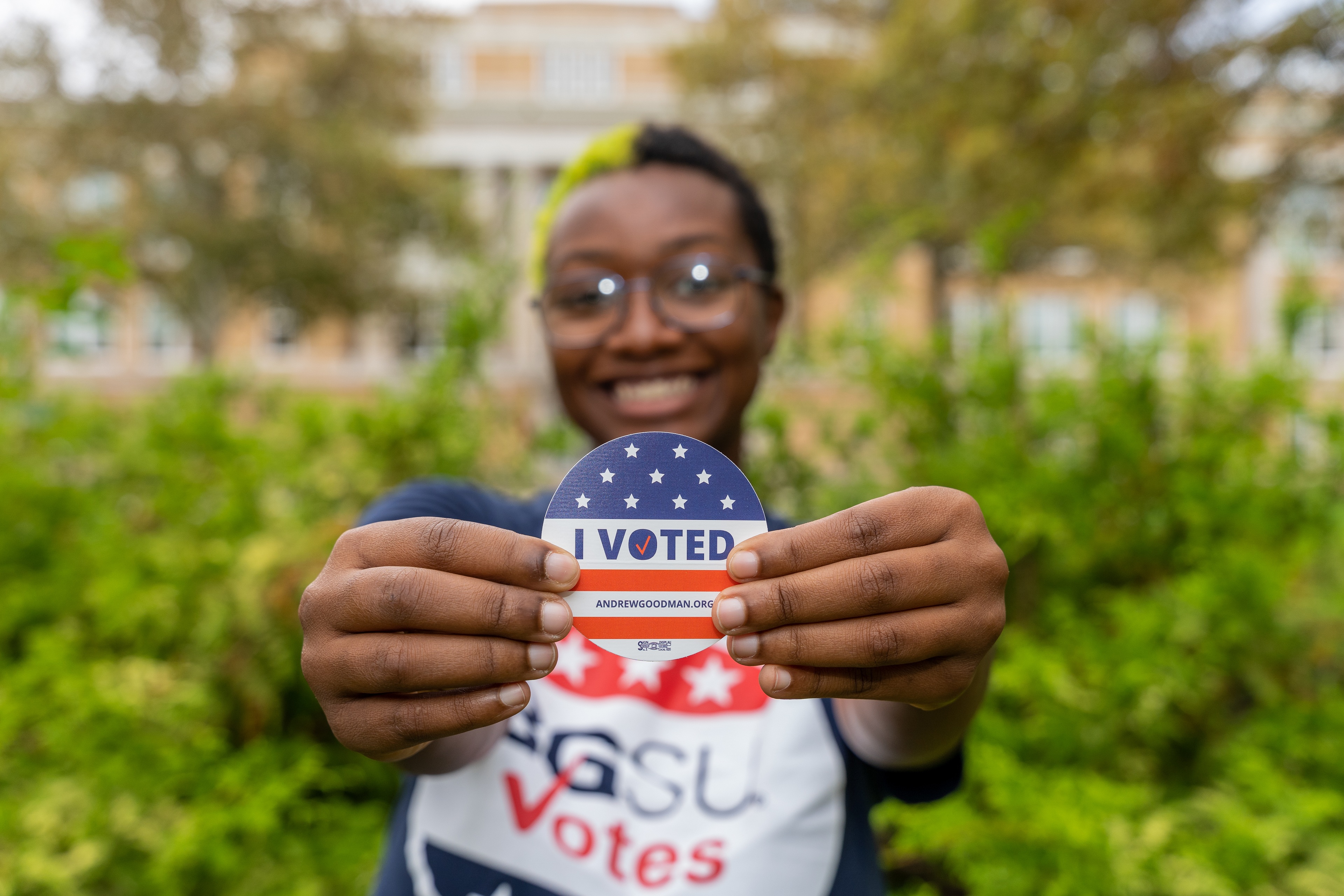 A person smiling while holding an "I Voted" sticker.