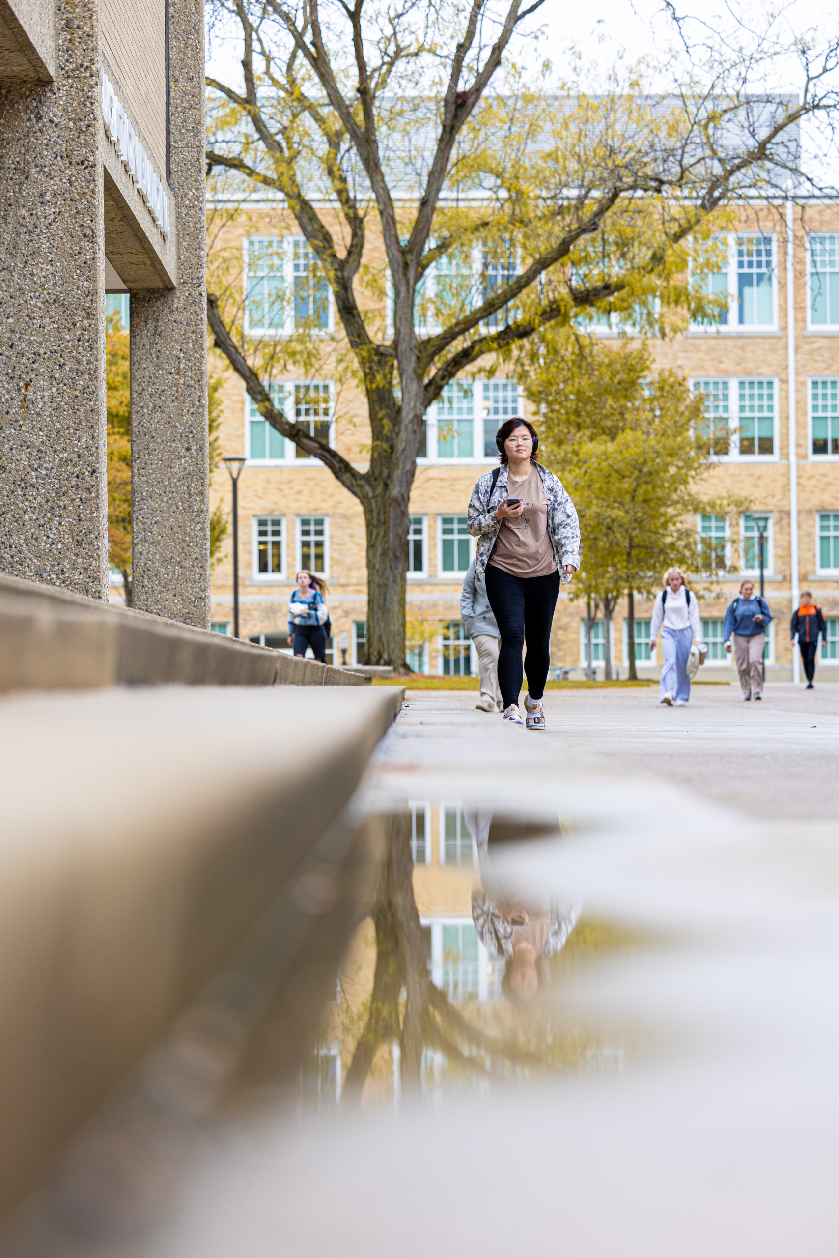 Student walking from class is reflected in a puddle outside the Education Building.