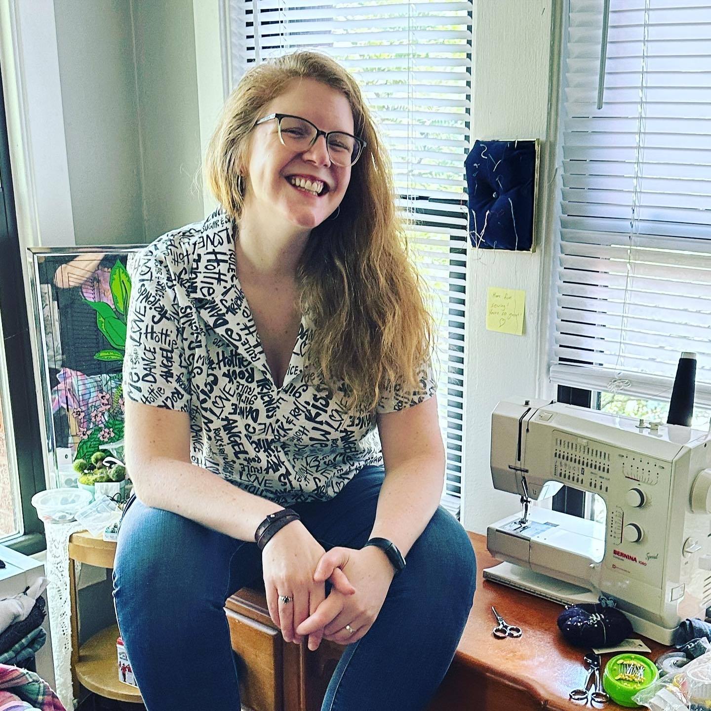 BGSU alumna Megan Grandstaff sits on a desk next to a sewing machine.