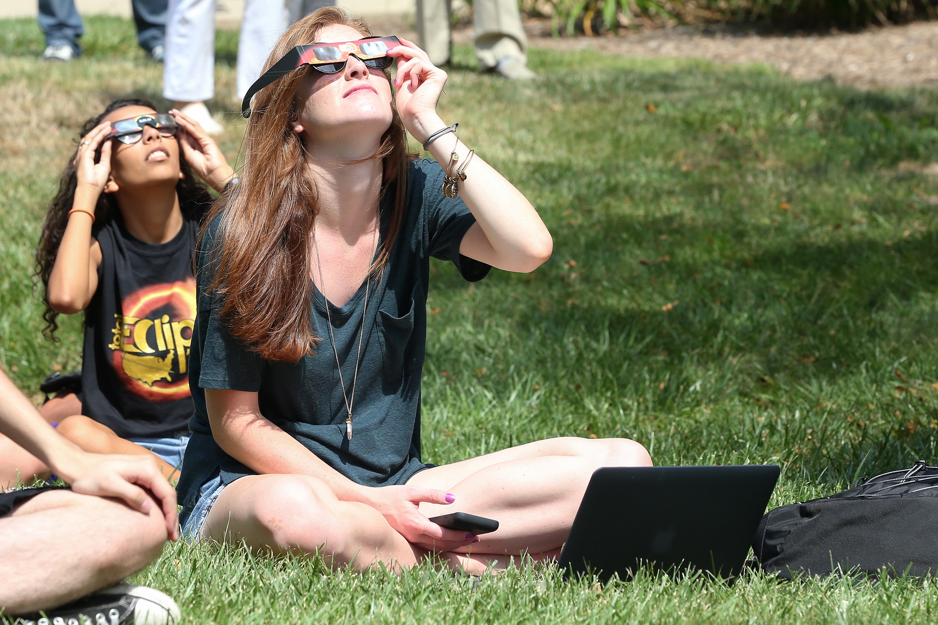 Two people wearing solar eclipse glasses gaze into the sky. 
