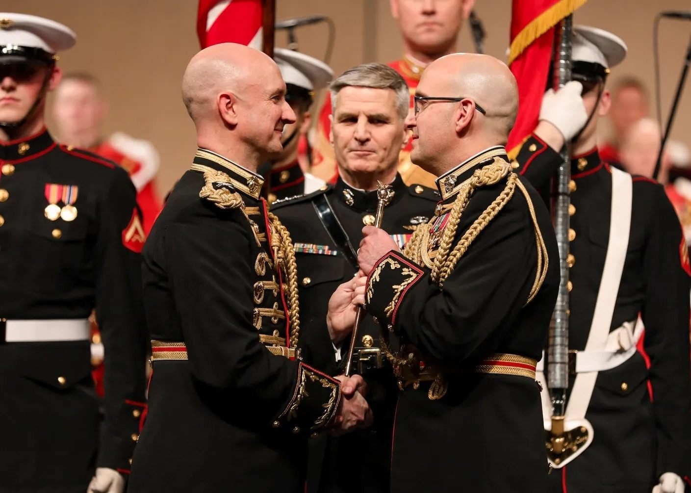 Three people in U.S. Marine dress uniform stand on stage