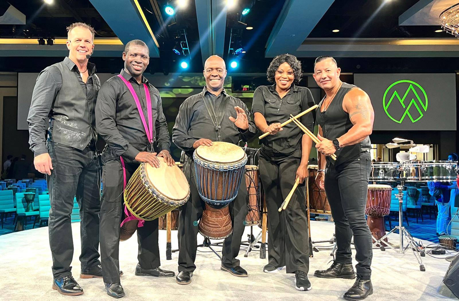 Dale Monnin stands on stage with four others holding drums during a group presentation in a large ballroom.