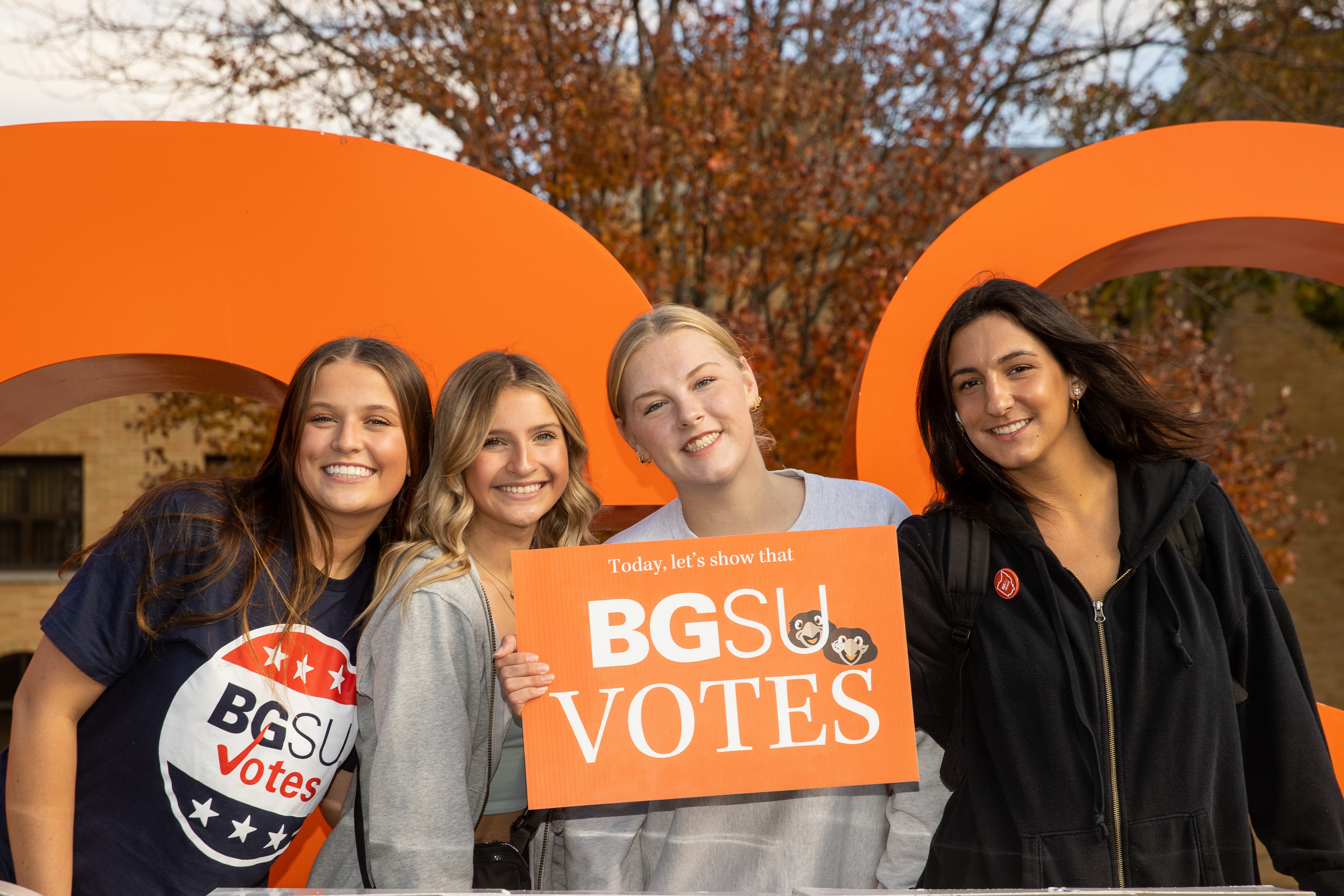 Four people smile at the camera while holding a sign that says BGSU Votes.