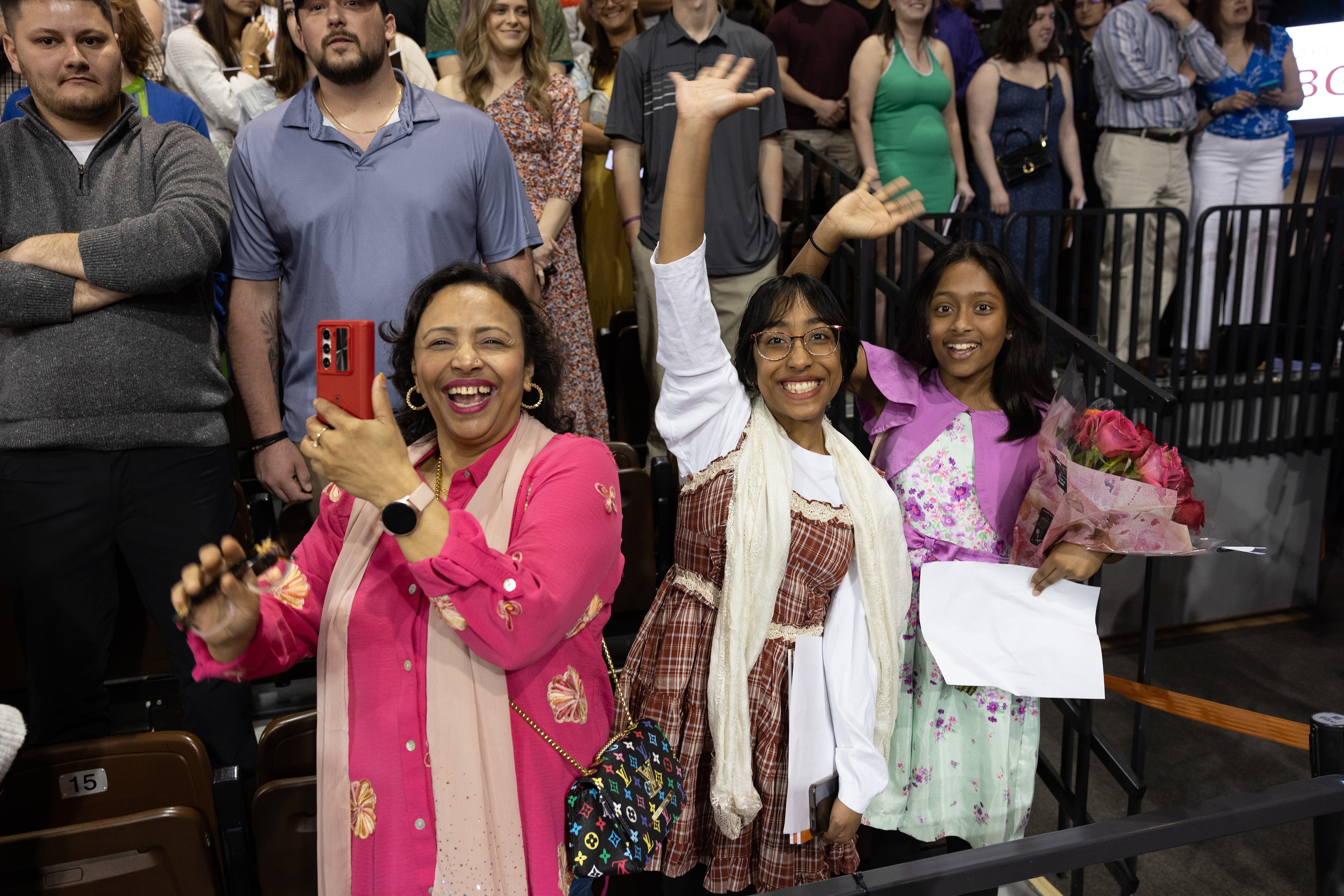 Three excited family members wave to their graduate from their seats.
