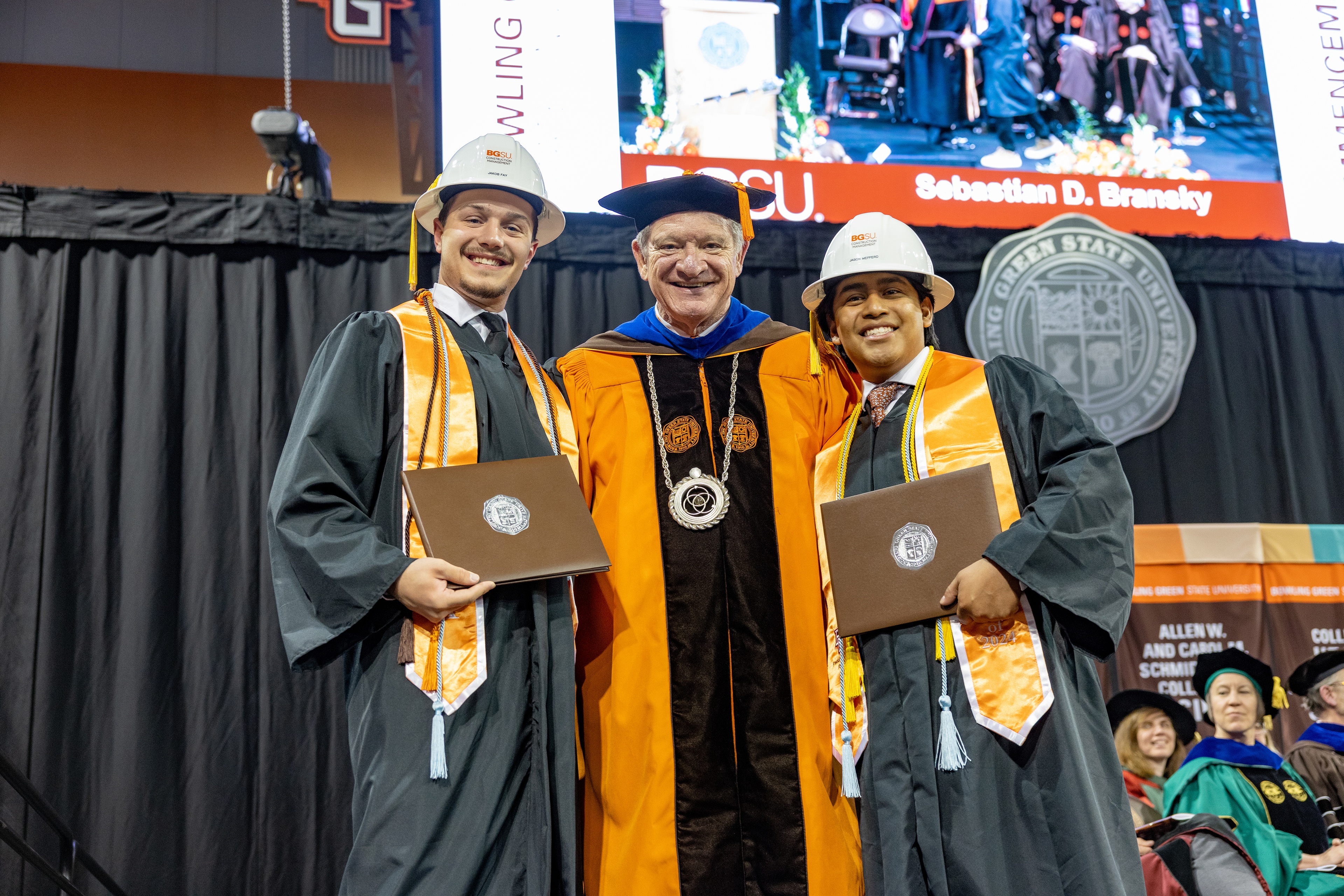 BGSU President Rodney K. Rogers poses for a photo with two graduates wearing hard hats