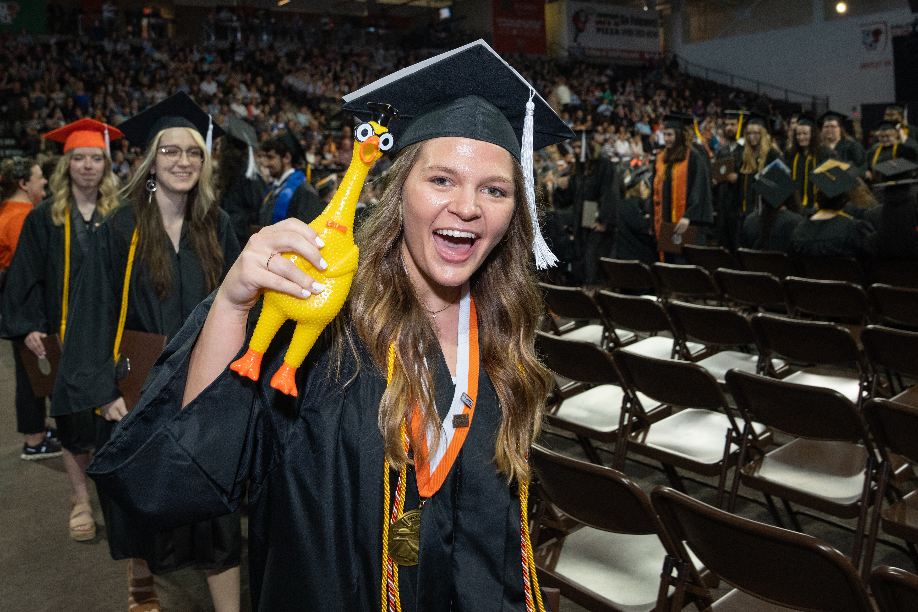 Female graduate holds a yellow rubber chicken with a graduation cap