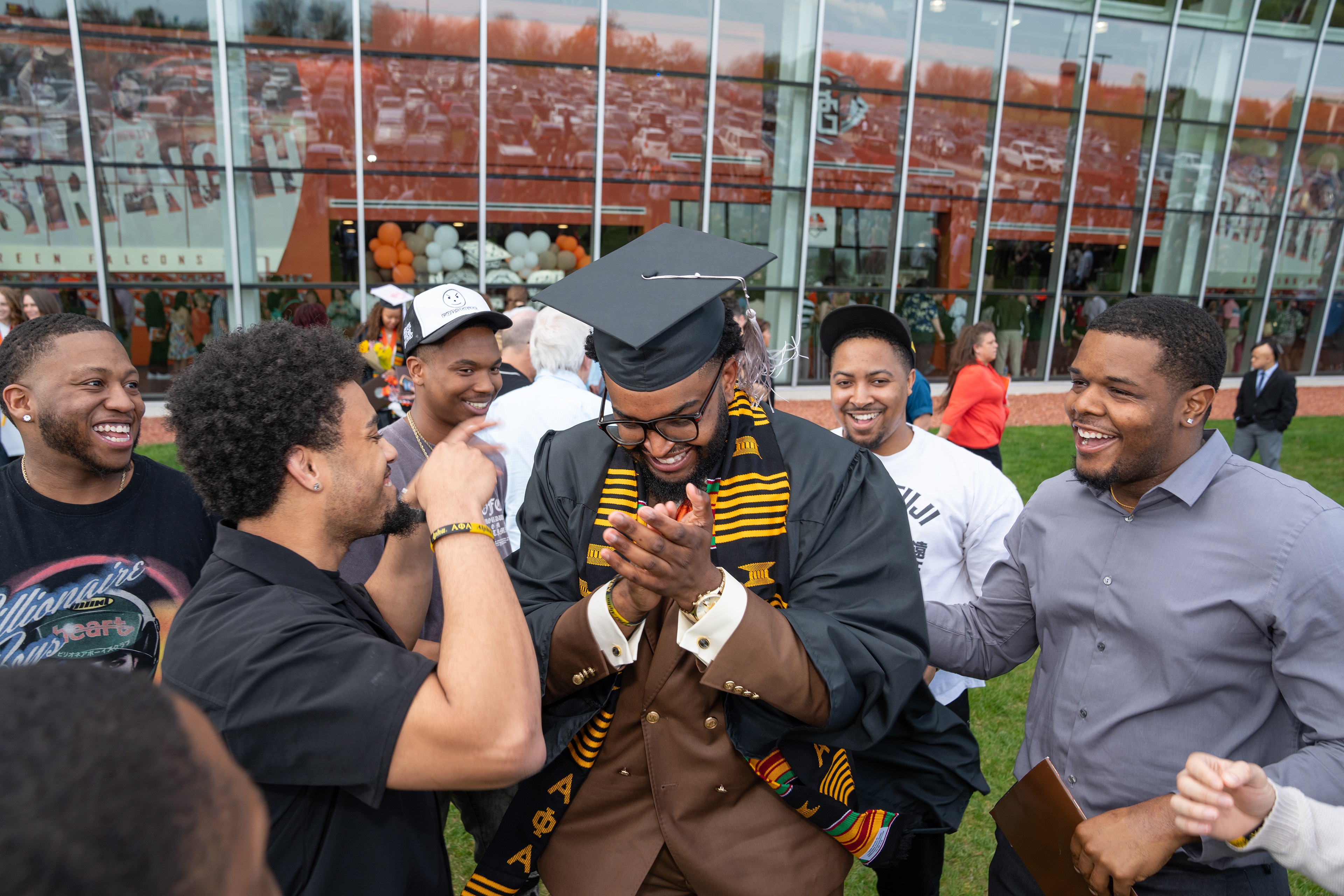 A graduate with a cap and gown smiles while friends congratulate him