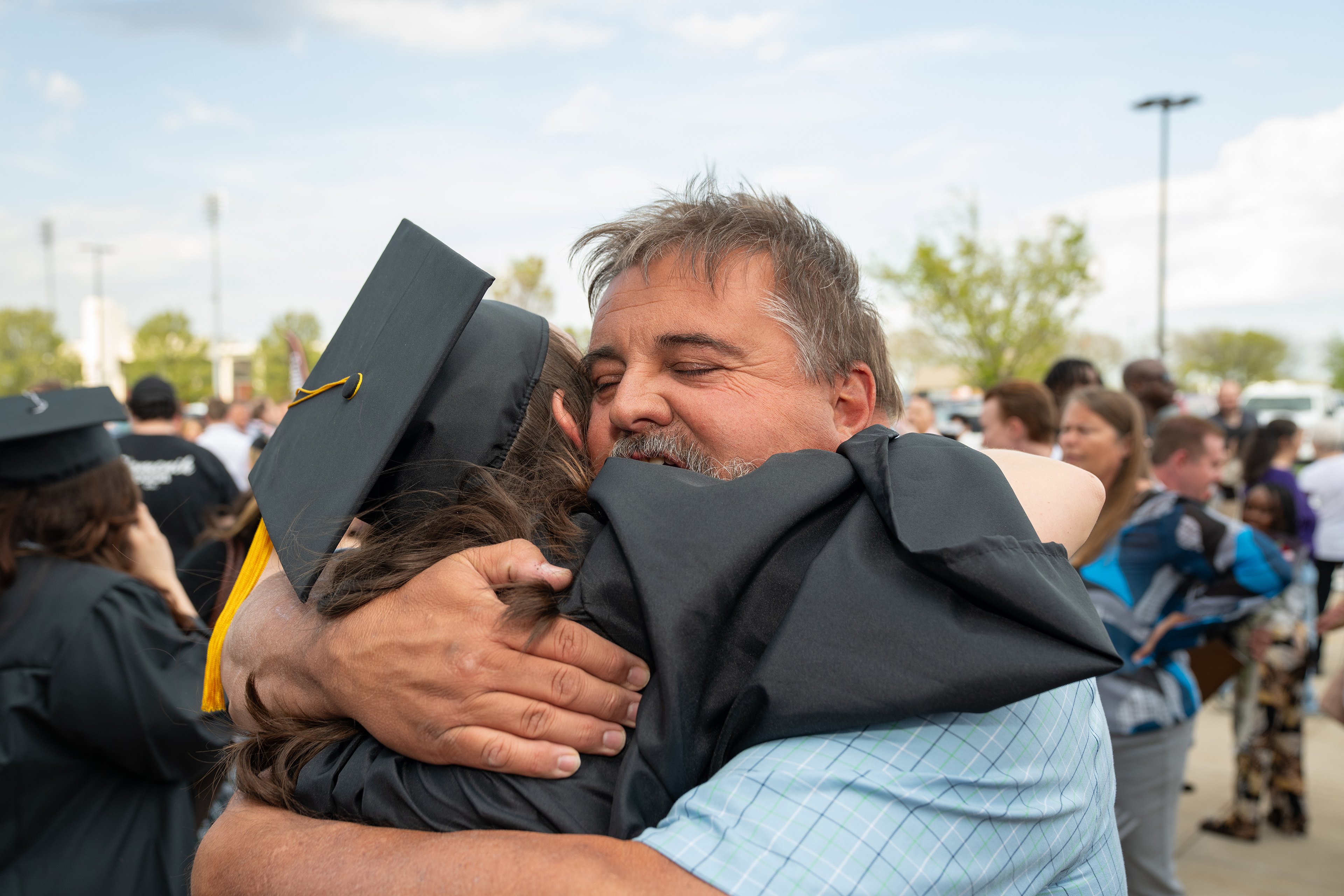 A man hugs a person in a graduation cap and gown