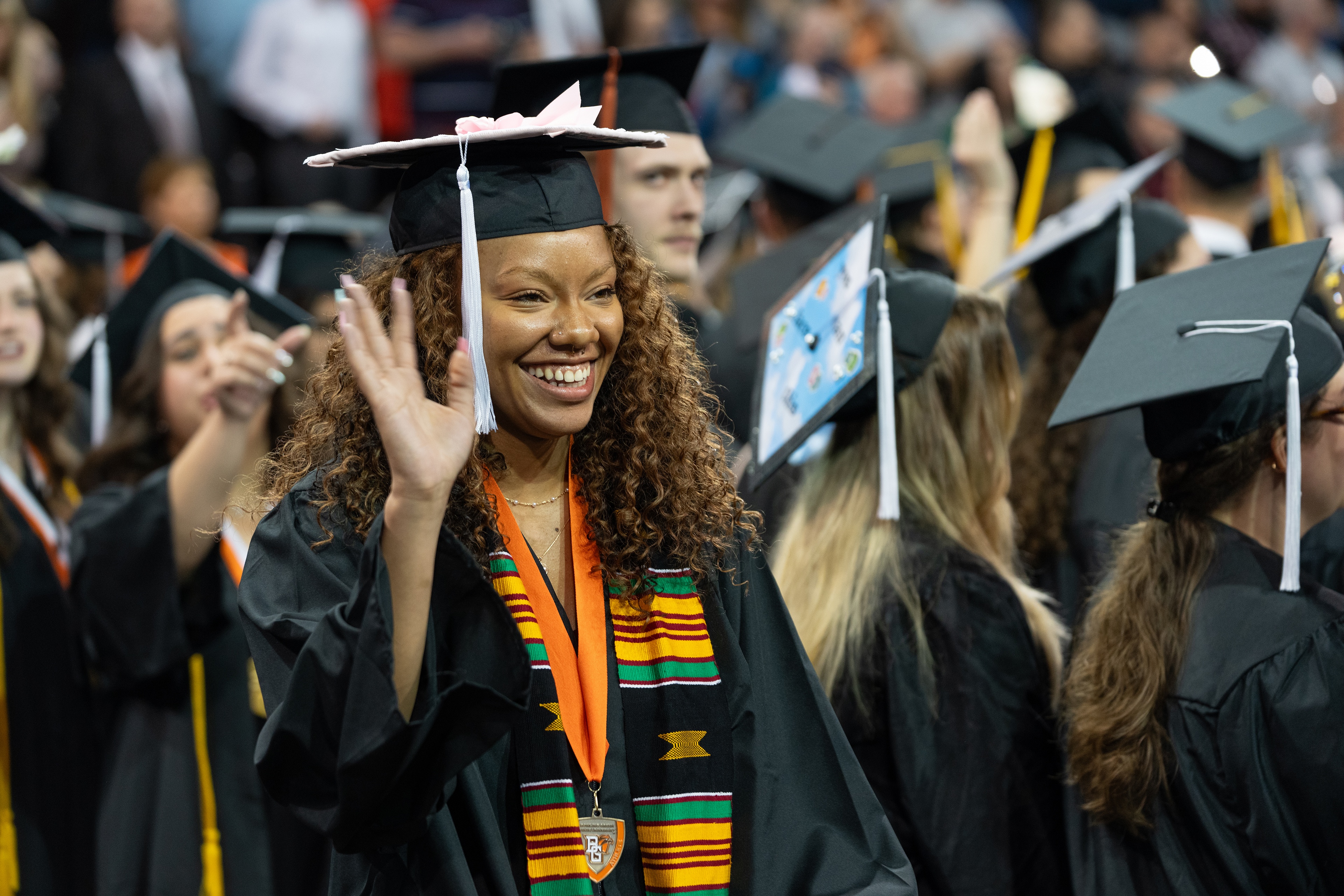 Young female graduate waves while wearing an African cloth stole
