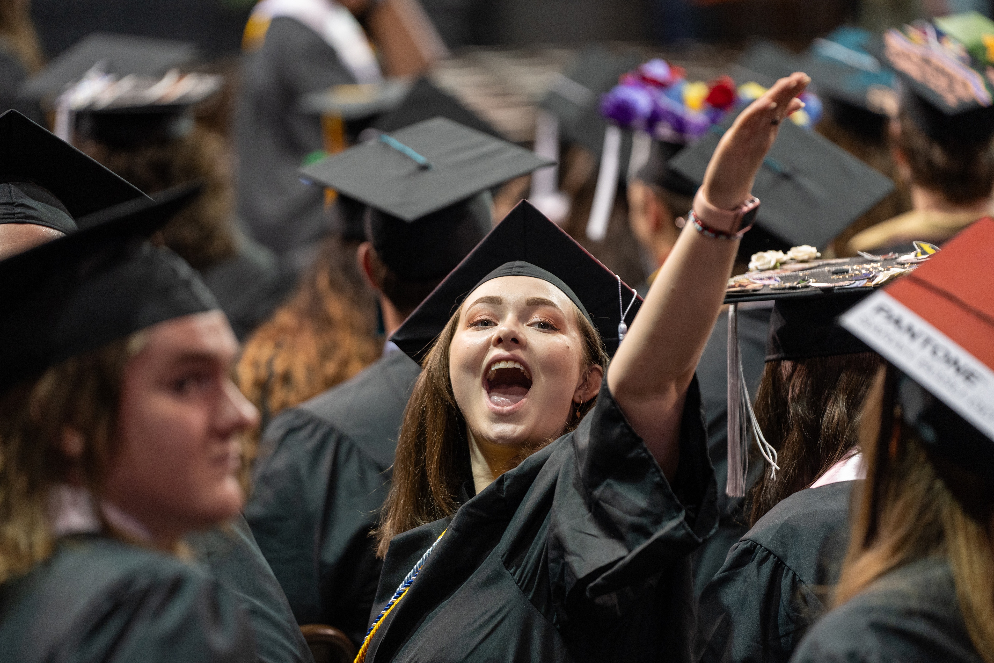 Young woman in graduation cap and gown with one arm raised 
