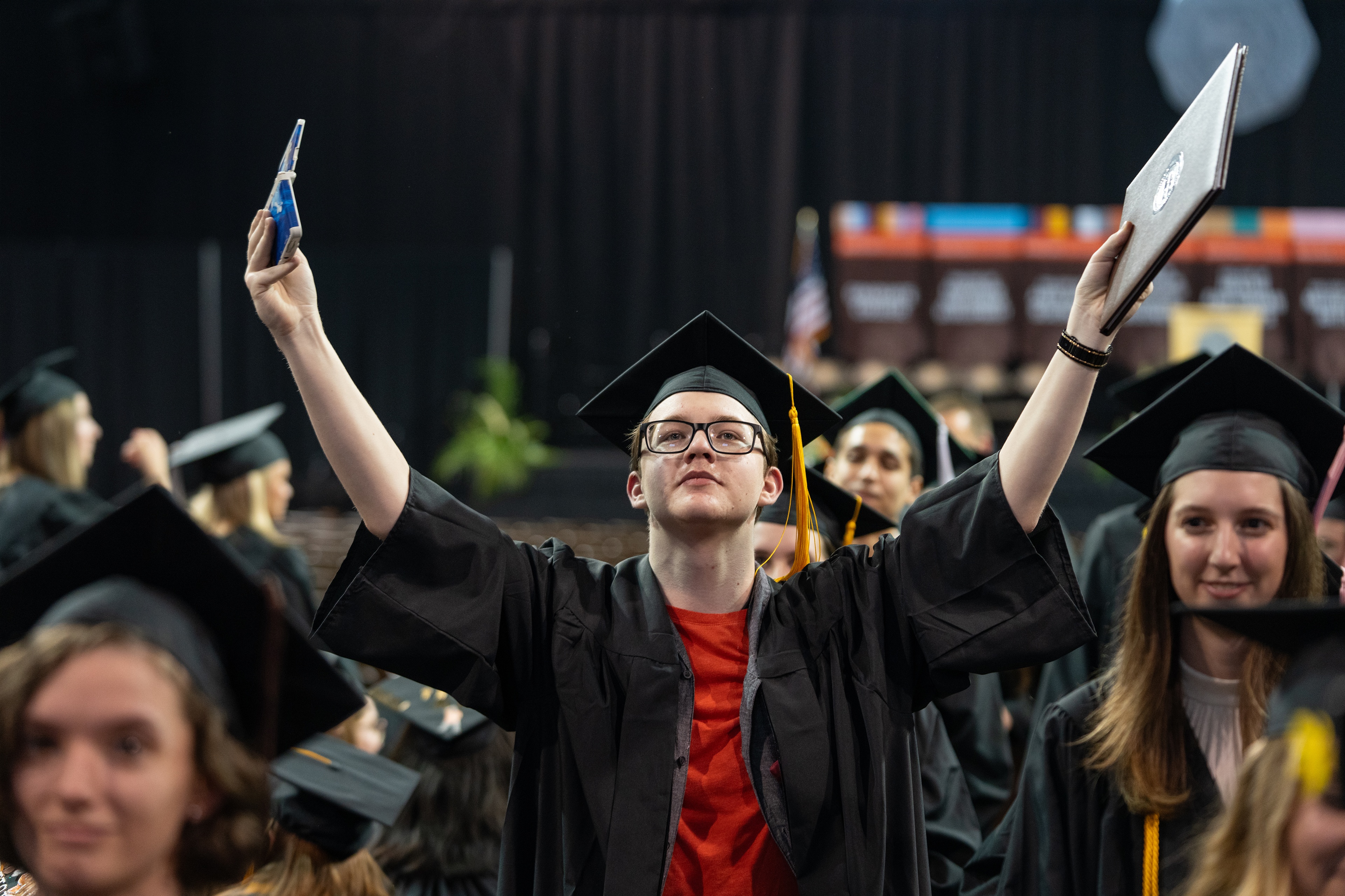 Young man in graduation cap and gown with arms raised