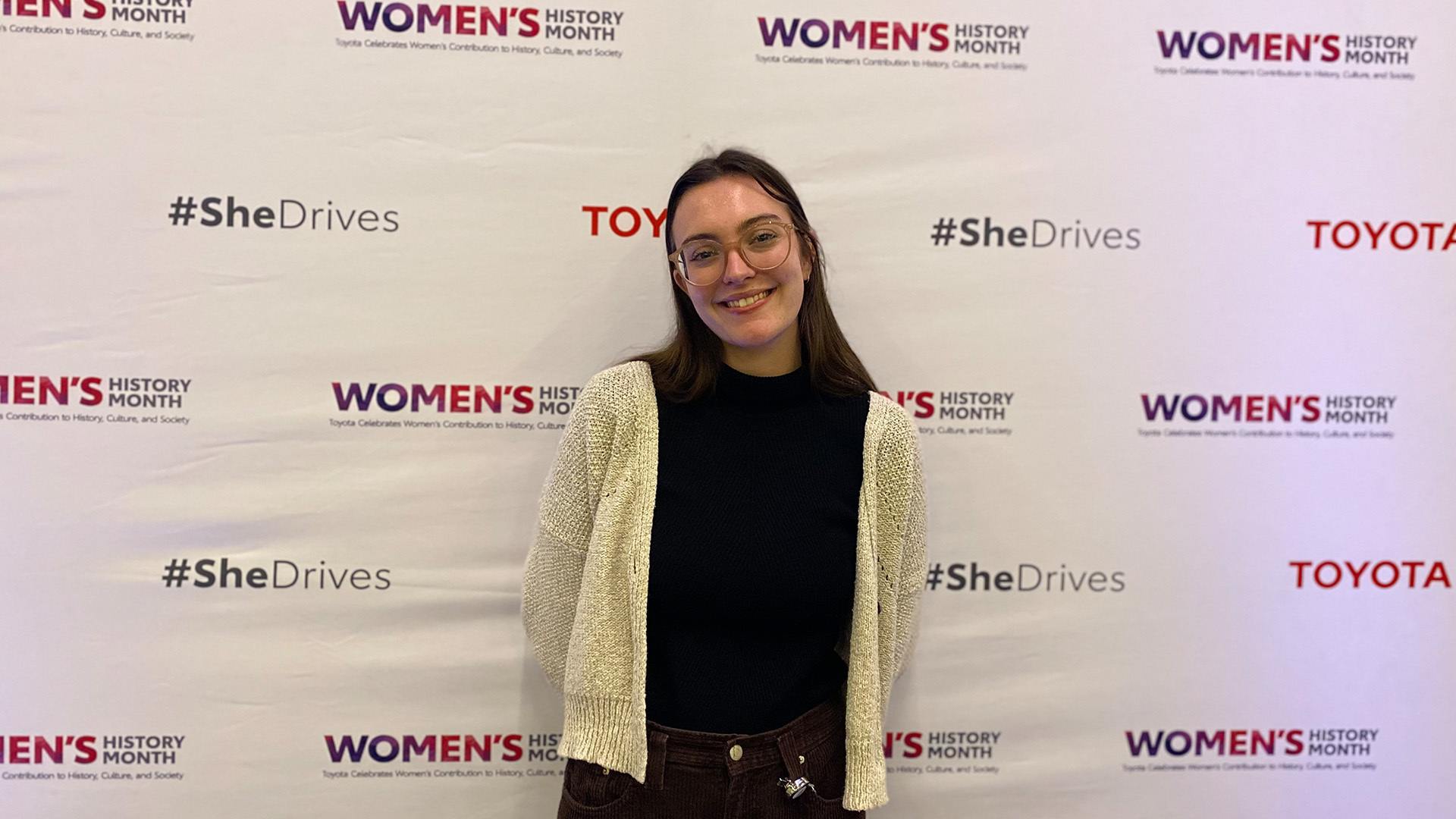 A person stands in front of a Toyota backdrop celebrating Women's History Month.