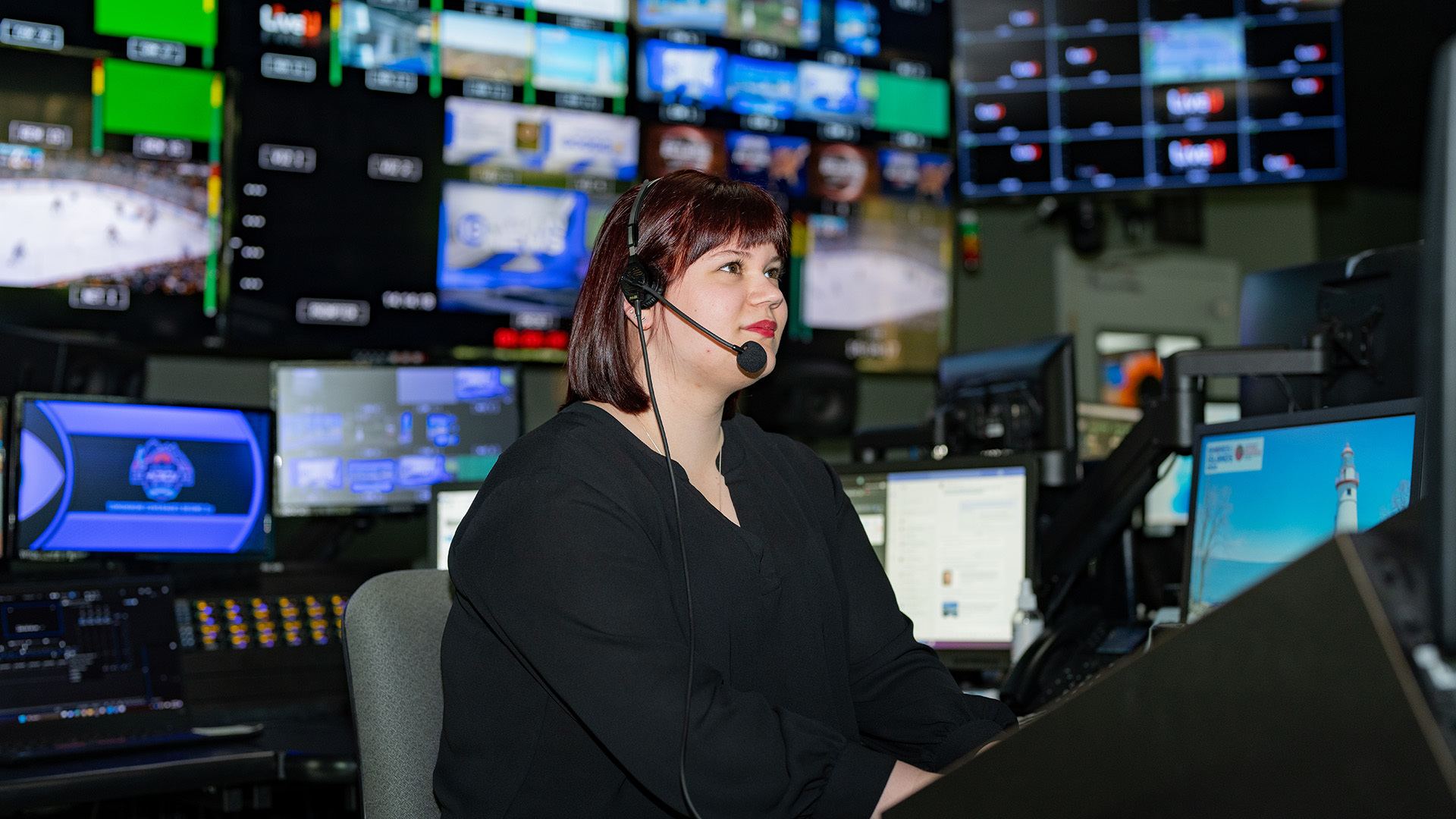 A person wearing a headset sits in a TV news control room.