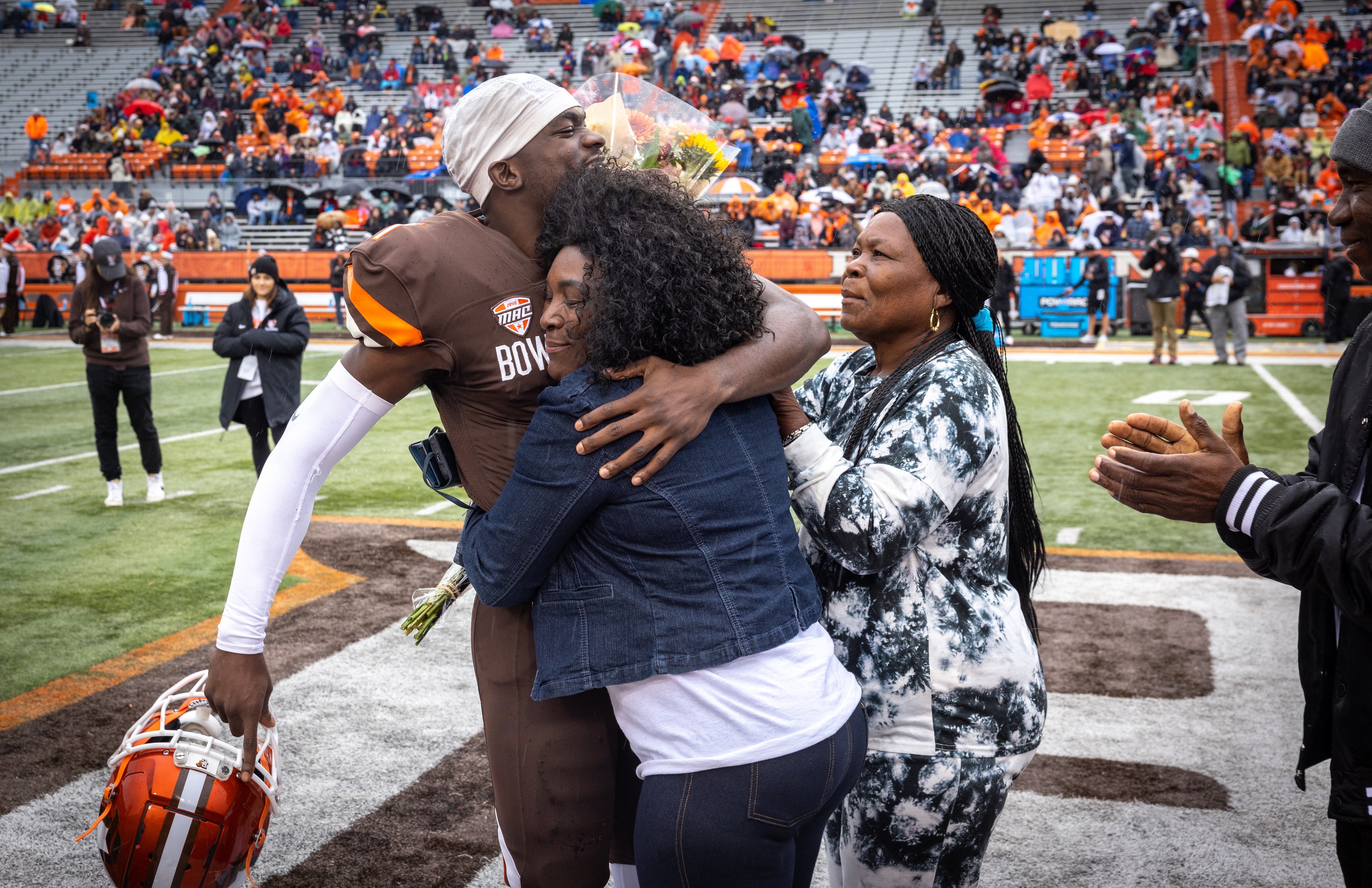 BGSU football player Odieu Hiliare hugs family members on the field at Doyt L. Perry Stadium. 