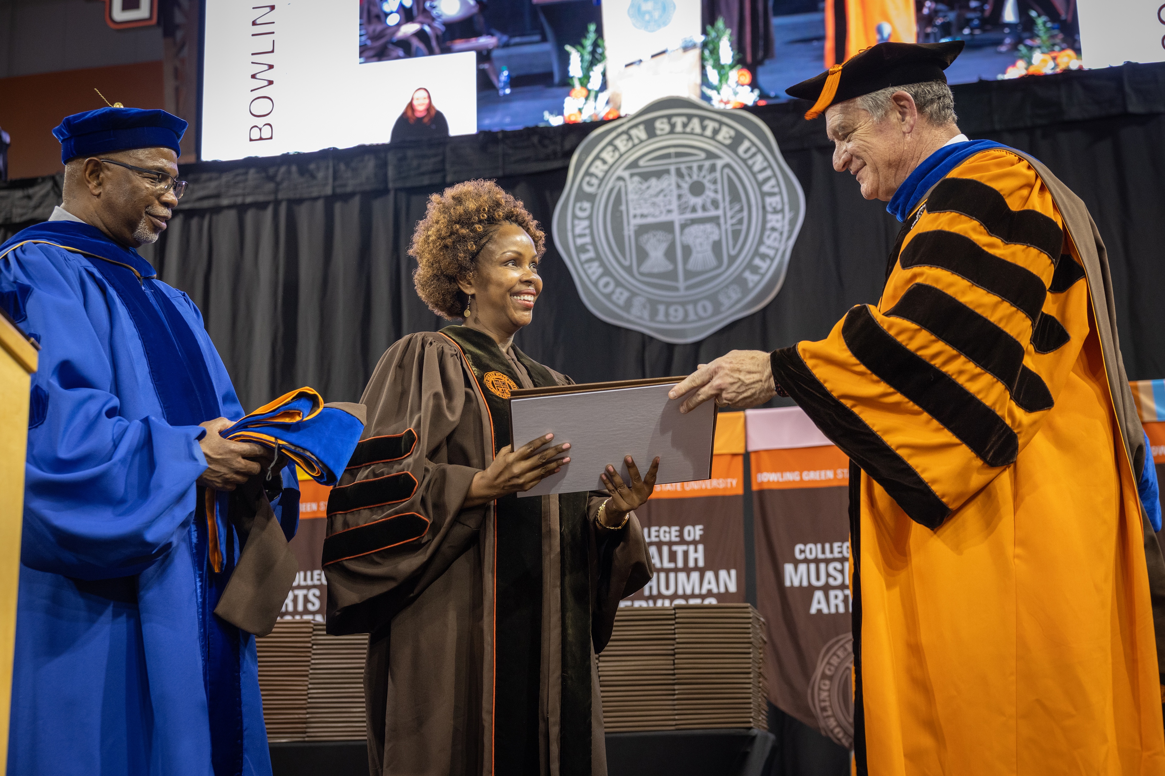 A woman accepts a framed document and graduation regalia from BGSU President Rodney K. Rogers and Provost Joe B. Whitehead Jr. 