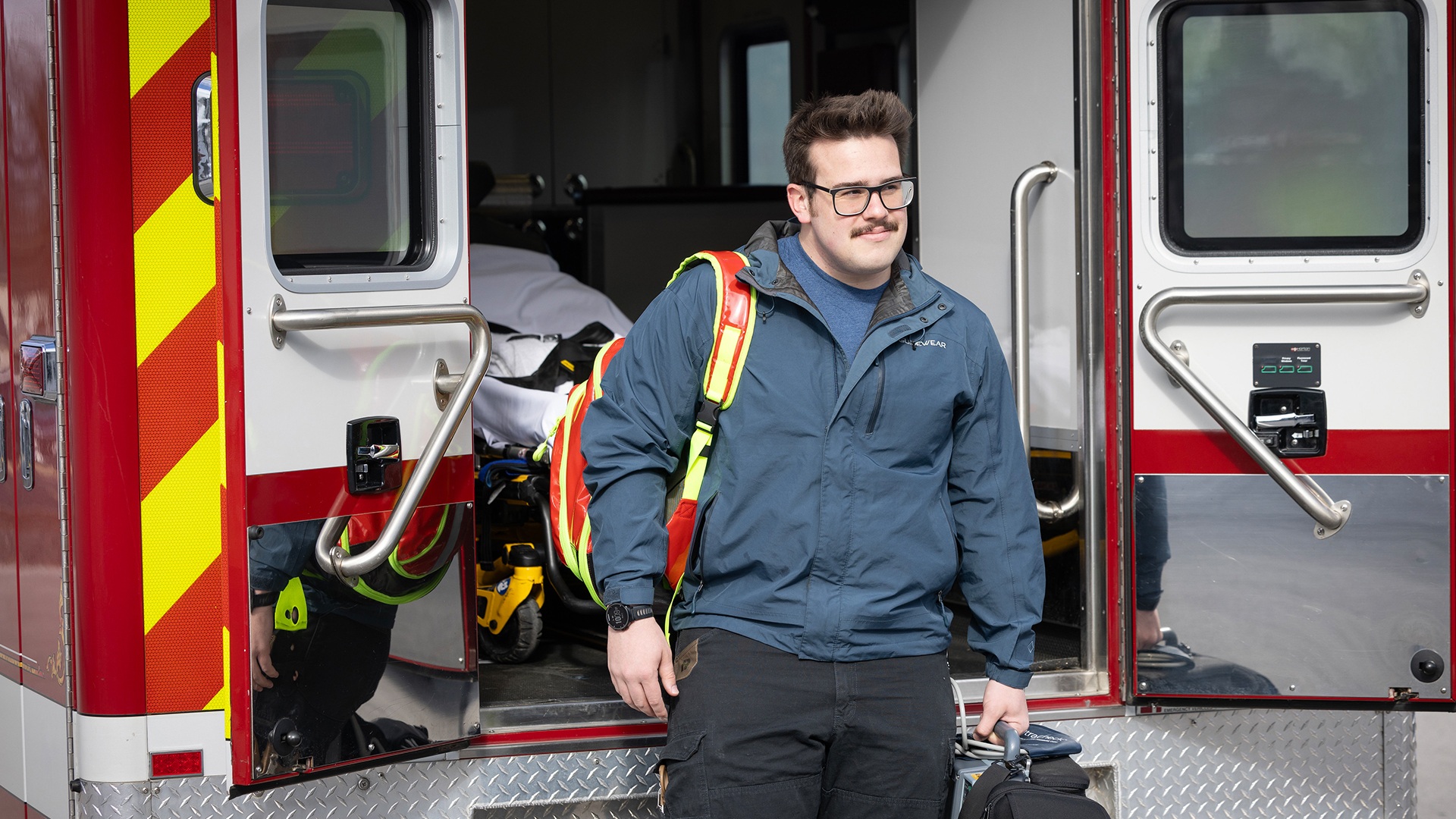 A person stands at the rear of an ambulance.