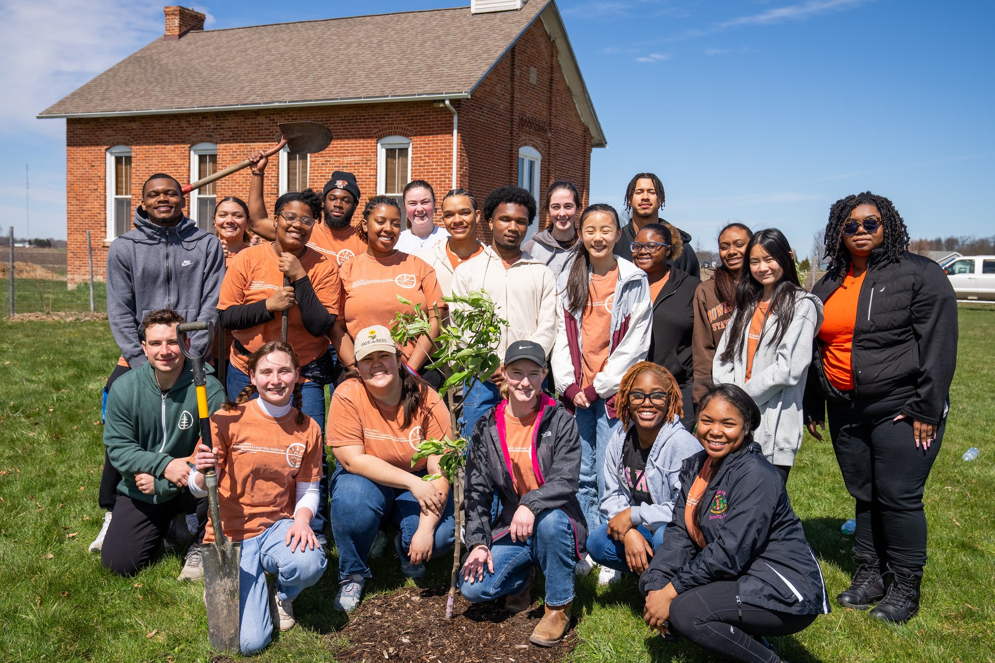 A group of smiling people gathered around a newly planted tree.