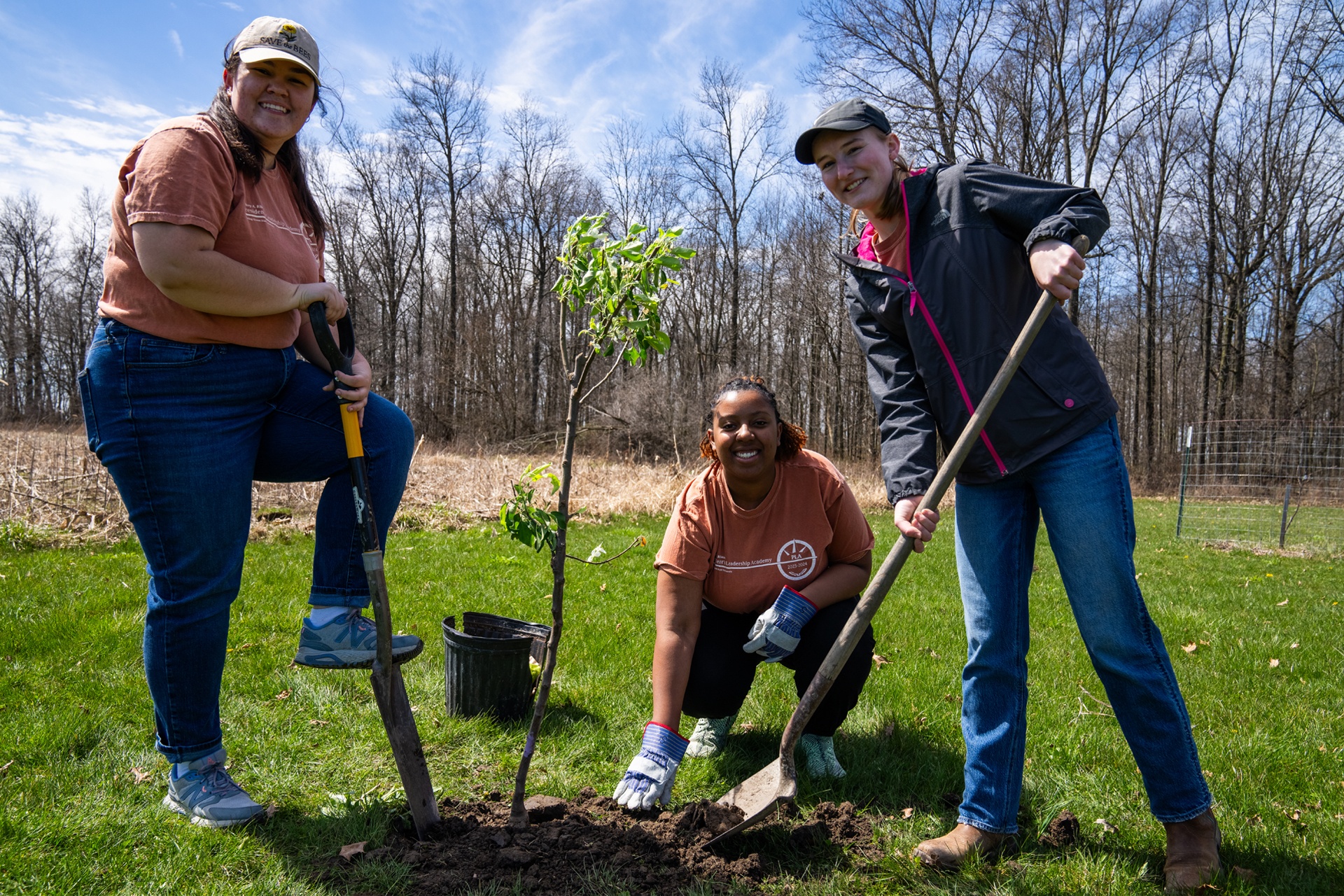 Three people smile after planting a tree at Carter Historic Farm in Bowling Green.