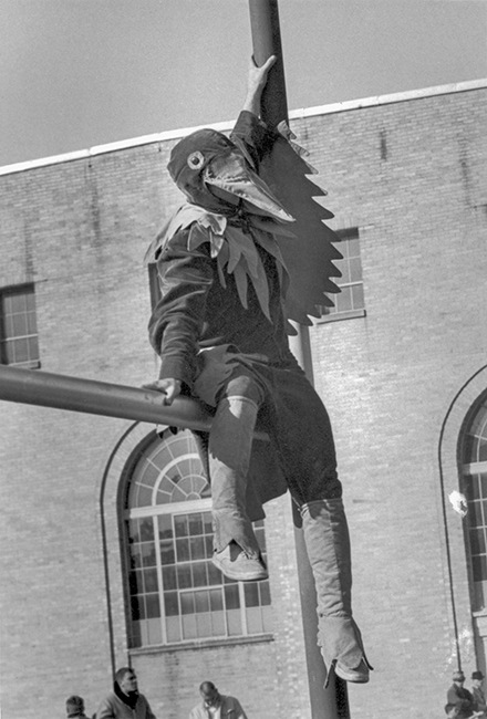 A person wearing a falcon costume sits on a field goal post