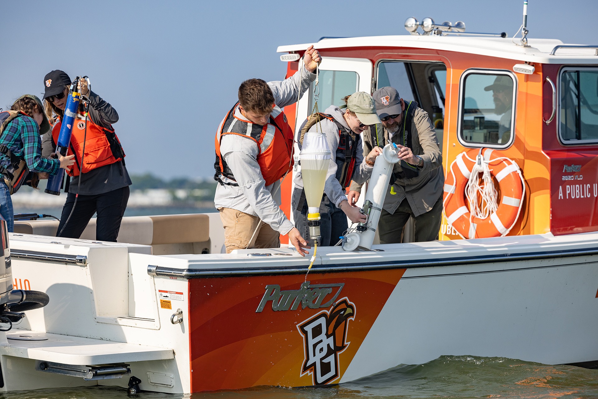 BGSU researchers collect water samples off the side of a boat
