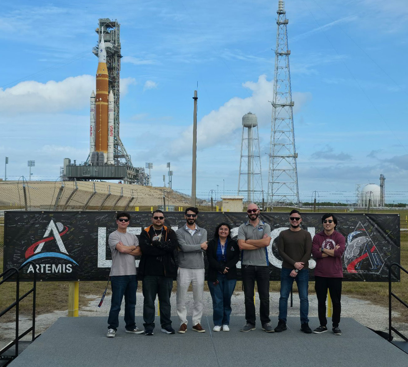 A group of people stand in front of the Artemis II spacecraft