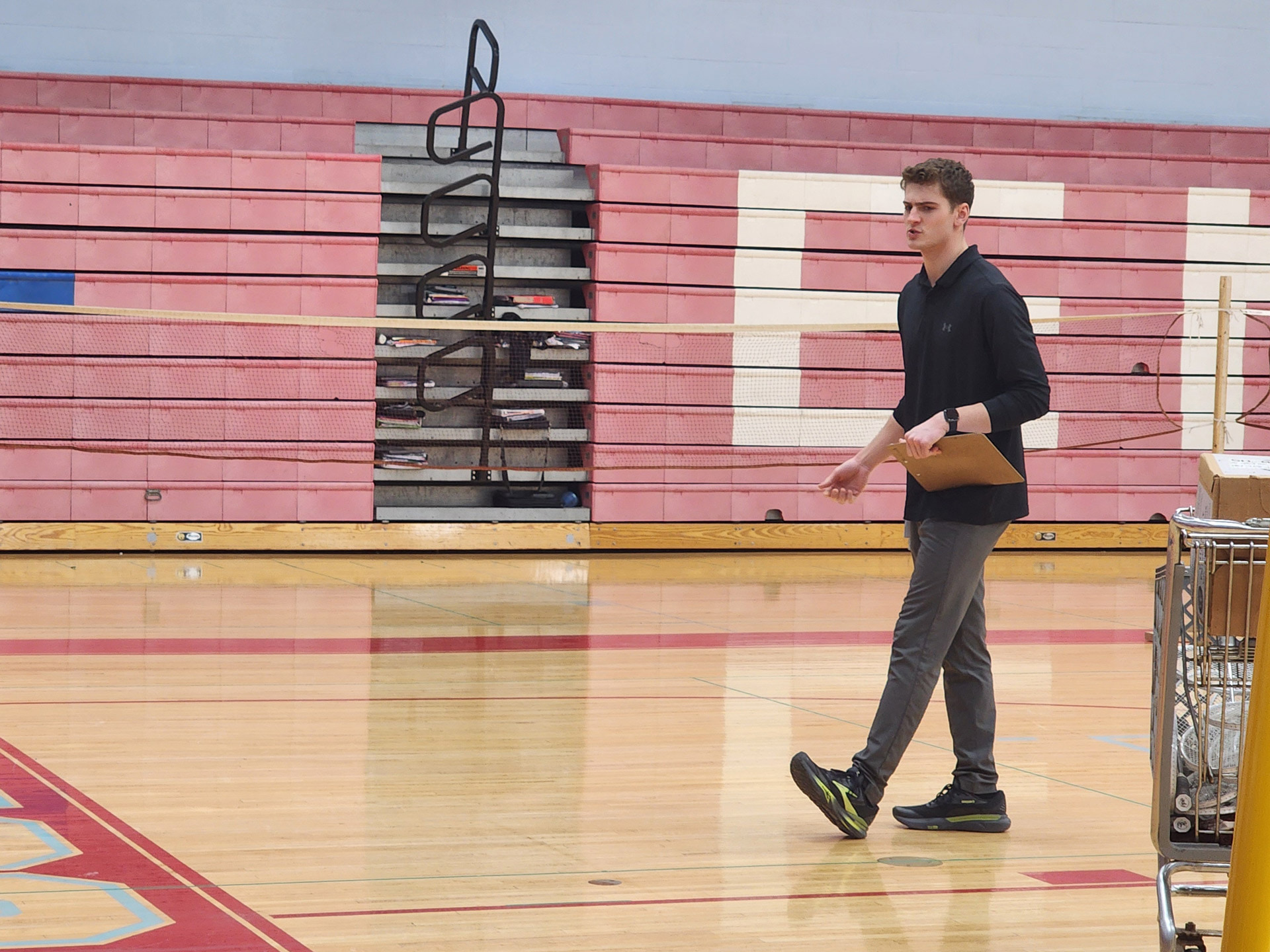 A gym teacher talks to students sitting on the floor.