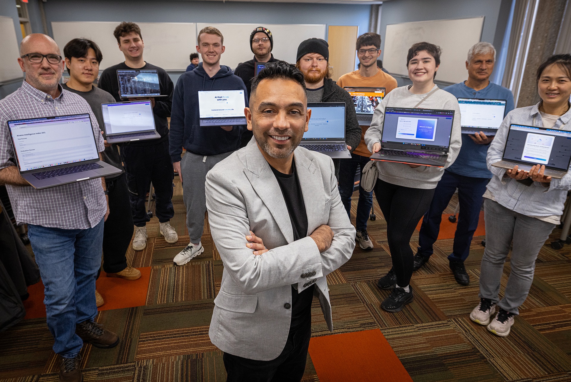 A person stands in the middle of a circle of people holding laptops
