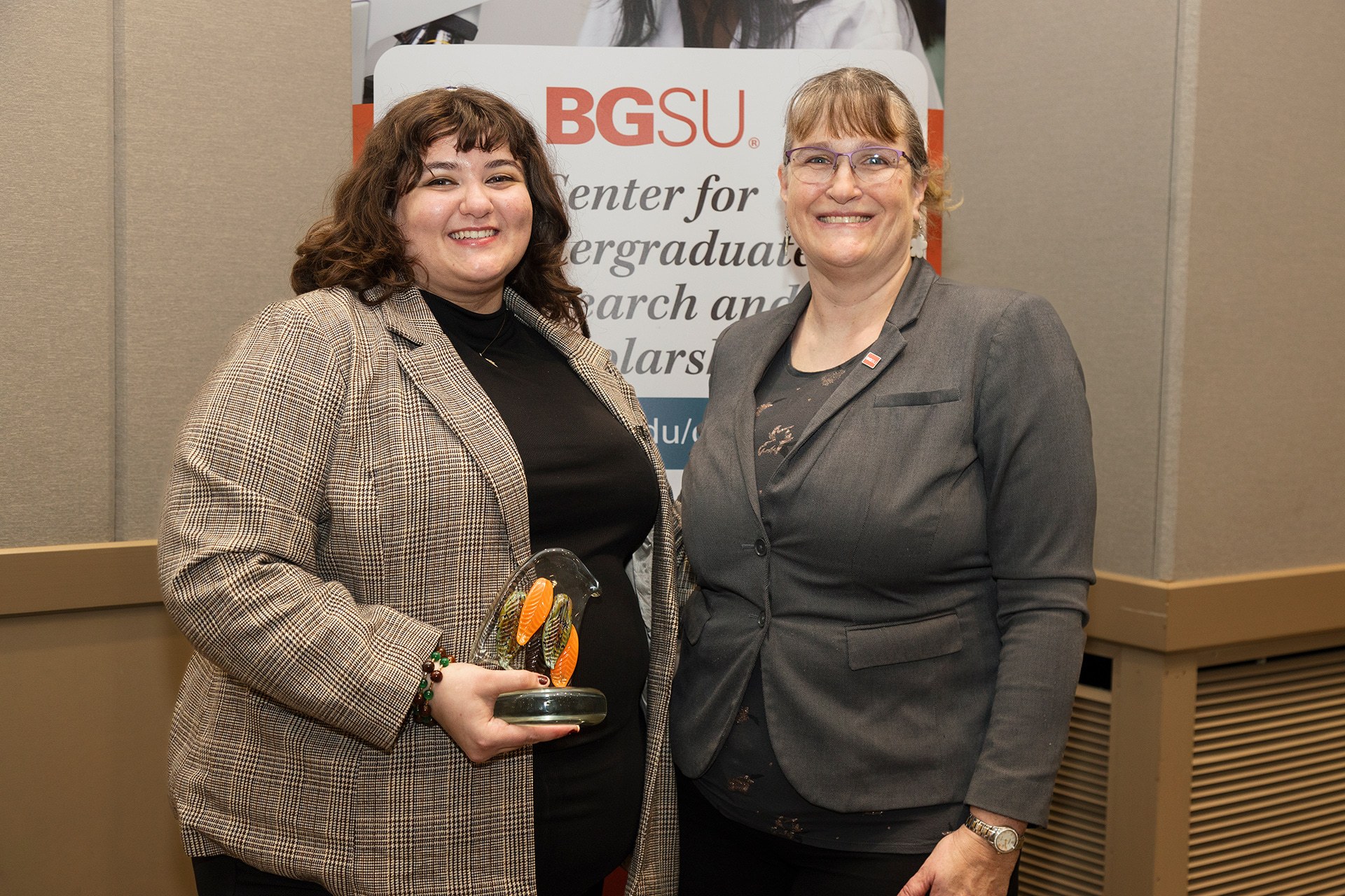 Two people pose for a photo as one holds a glass trophy.