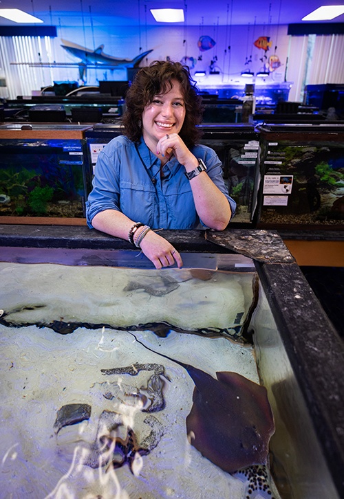 A person smiles near a fish tank with a stingray.
