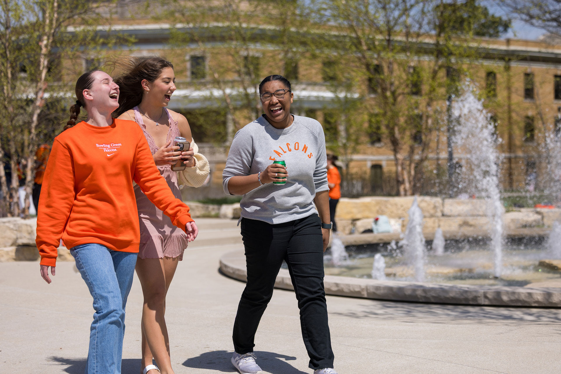 Three students laugh while walking outside.