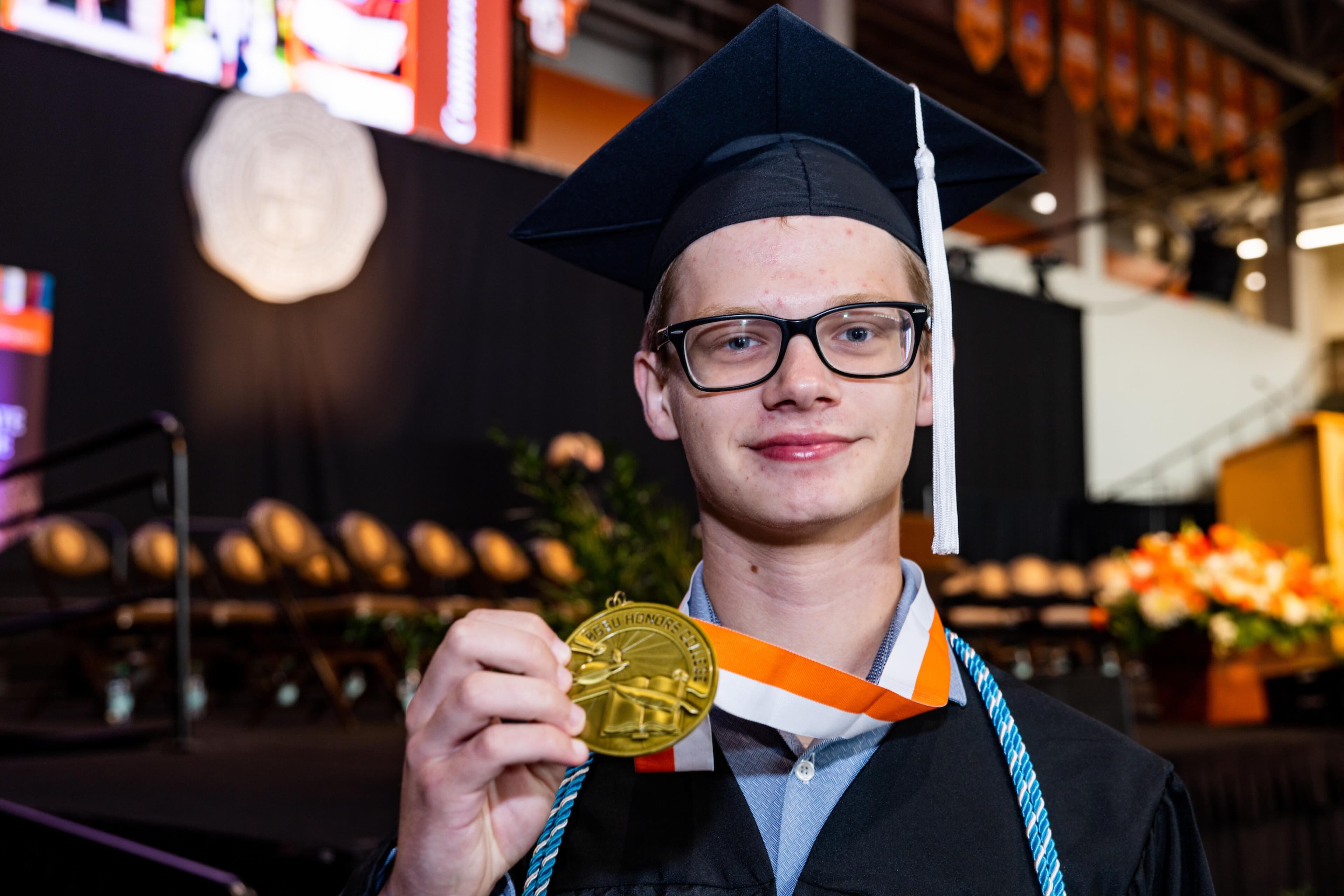 A BGSU graduate holds up his Honors College medallion