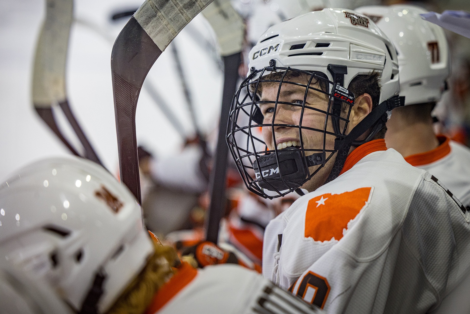A hockey player smiles on the bench.