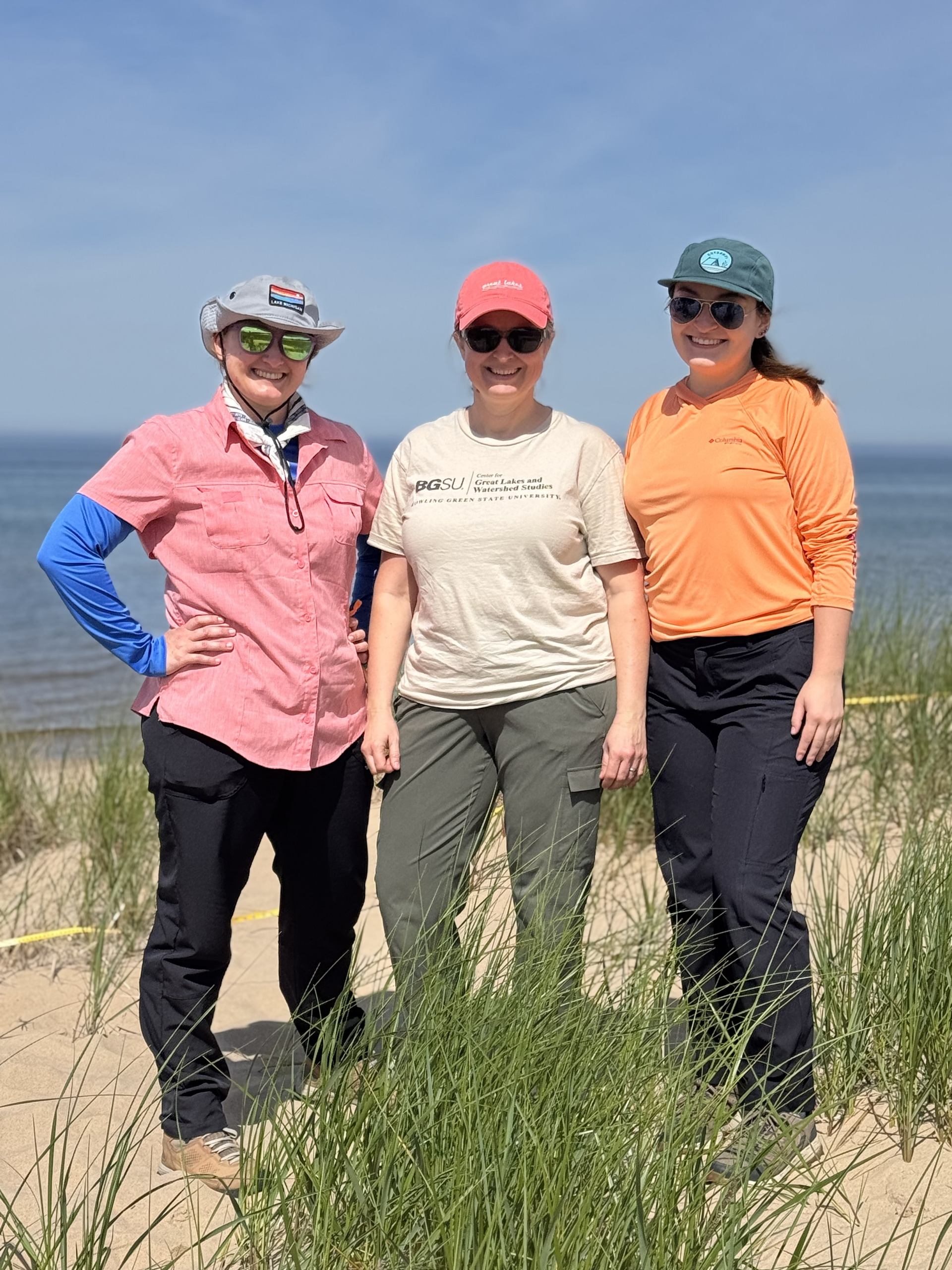 Three scientists pose on a sandy beach.