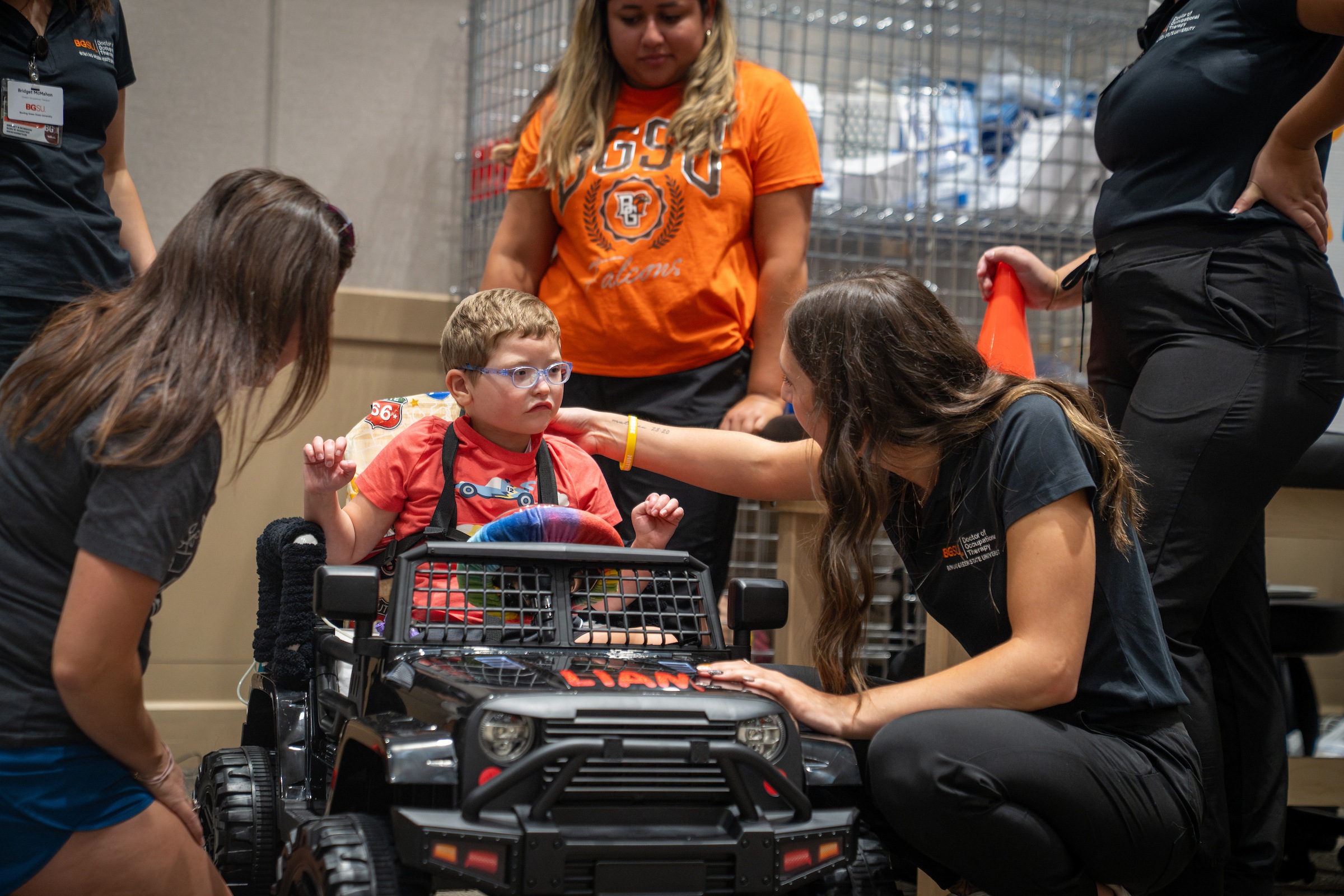 A BGSU student kneels to talk to a child in a toy car.