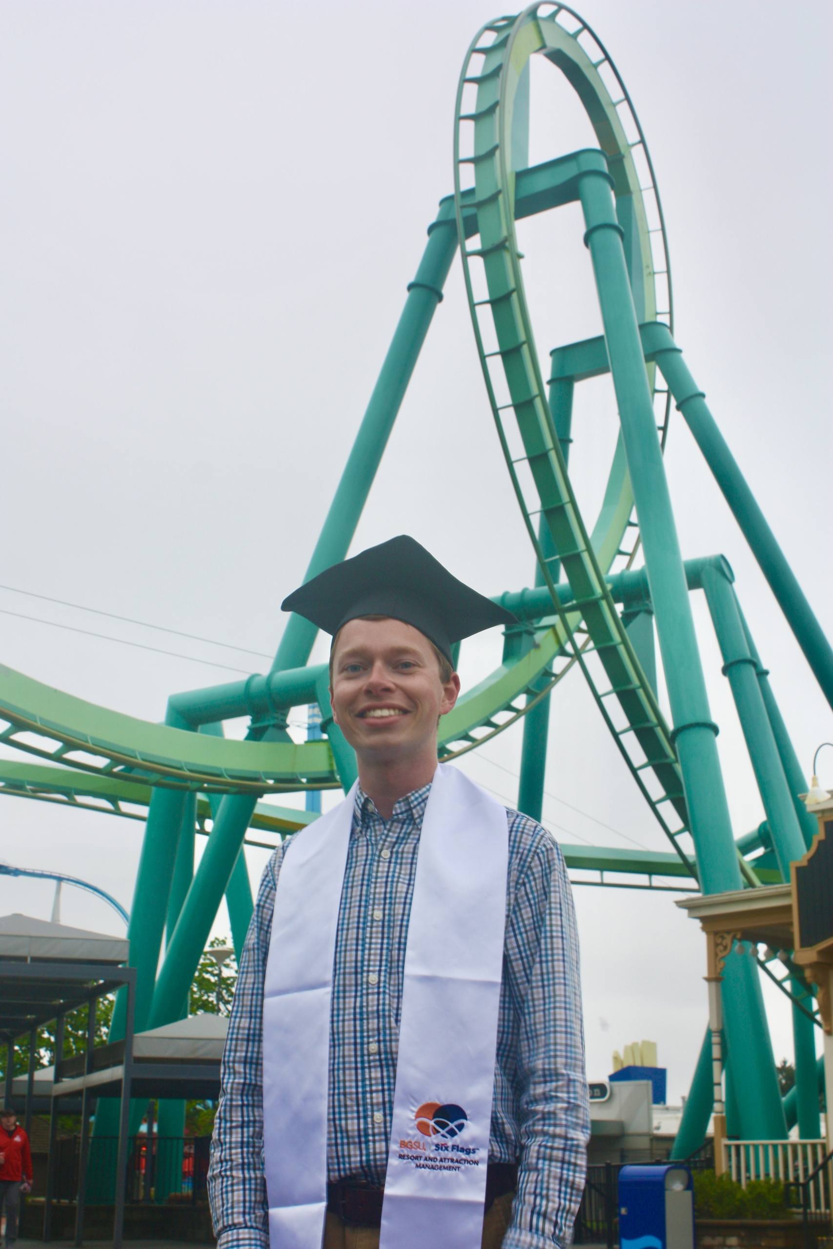 A person stands in front of a roller coaster.