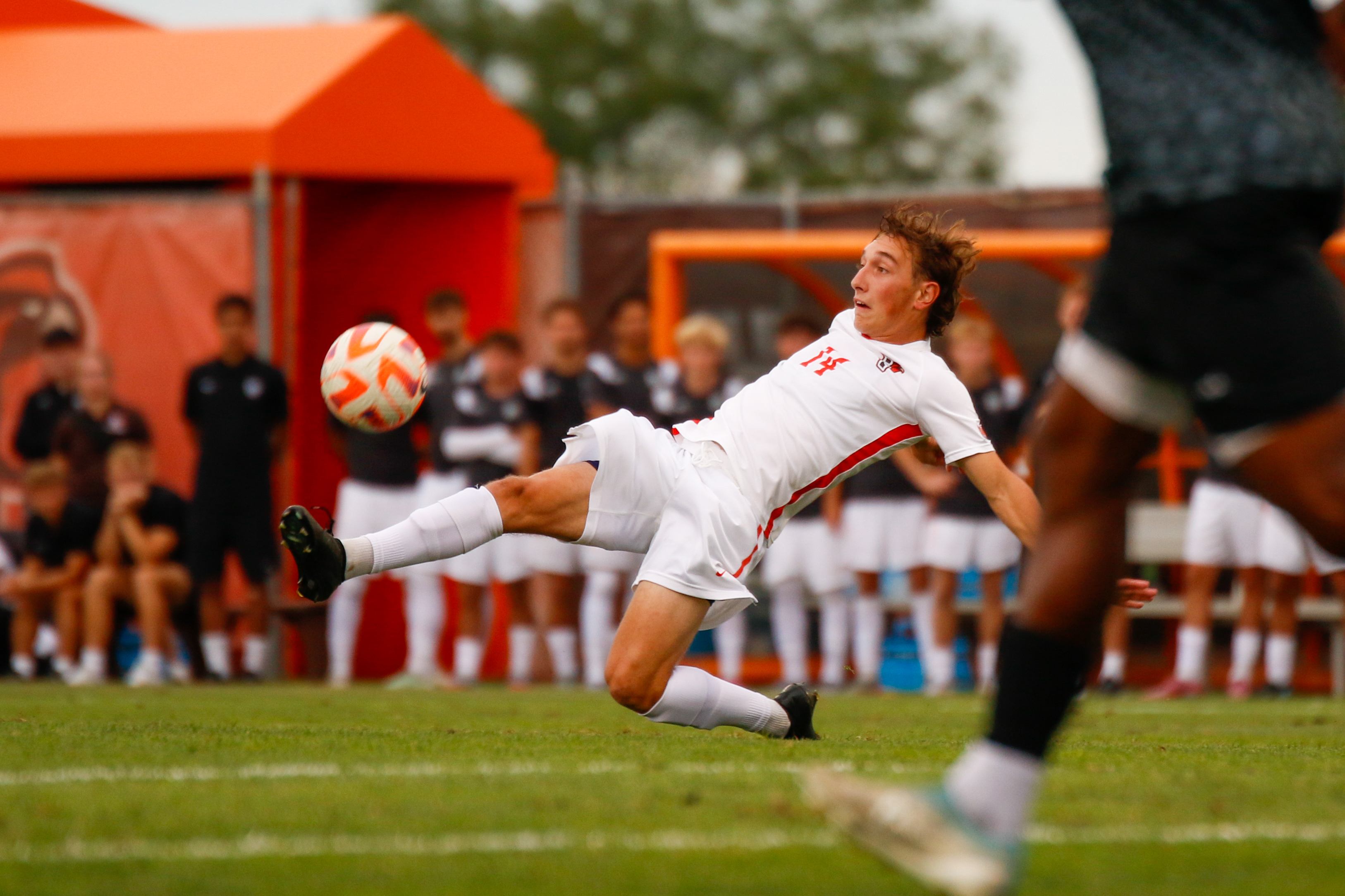 A soccer player leaps to kick a ball.
