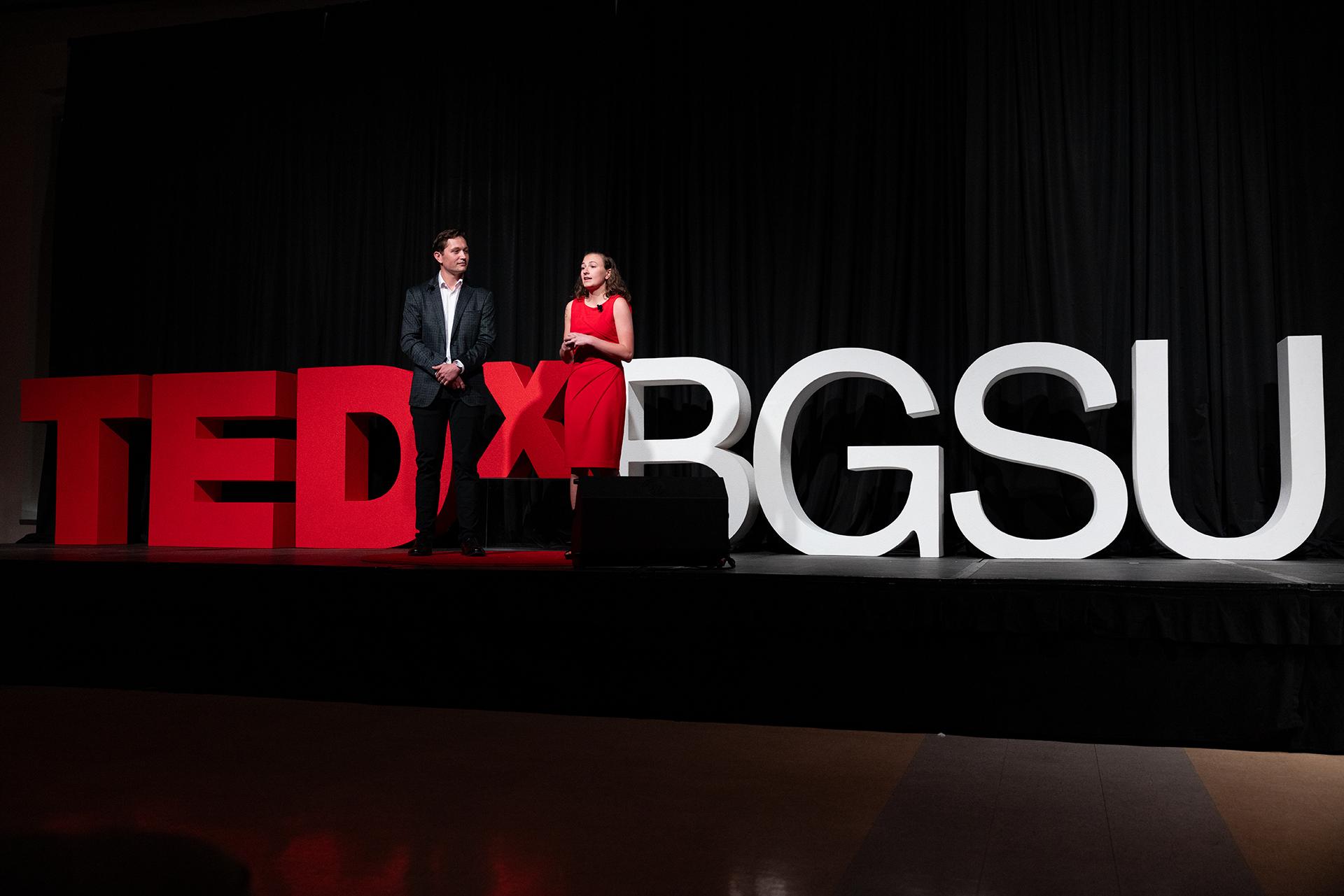 Two people stand on stage with the letters "TEDxBGSU" in the background.