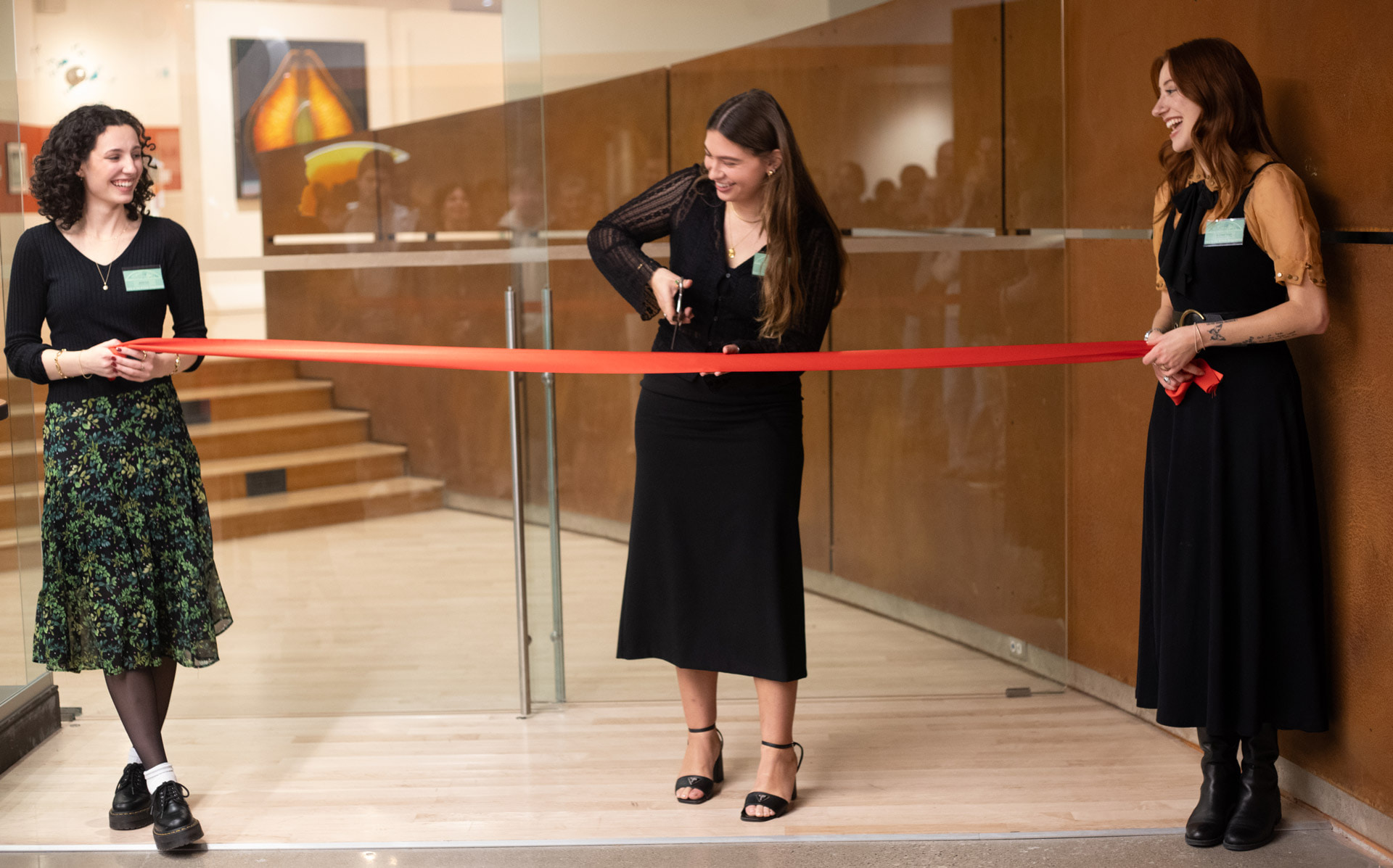 Two people hold a ribbon while a third person uses scissors to cut it. 