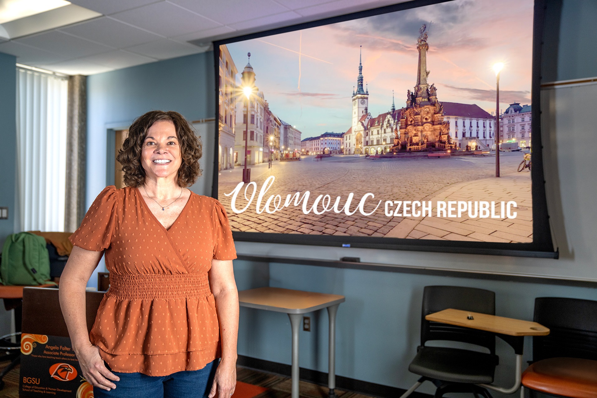 A teacher poses for a photo in front of a projector screen.