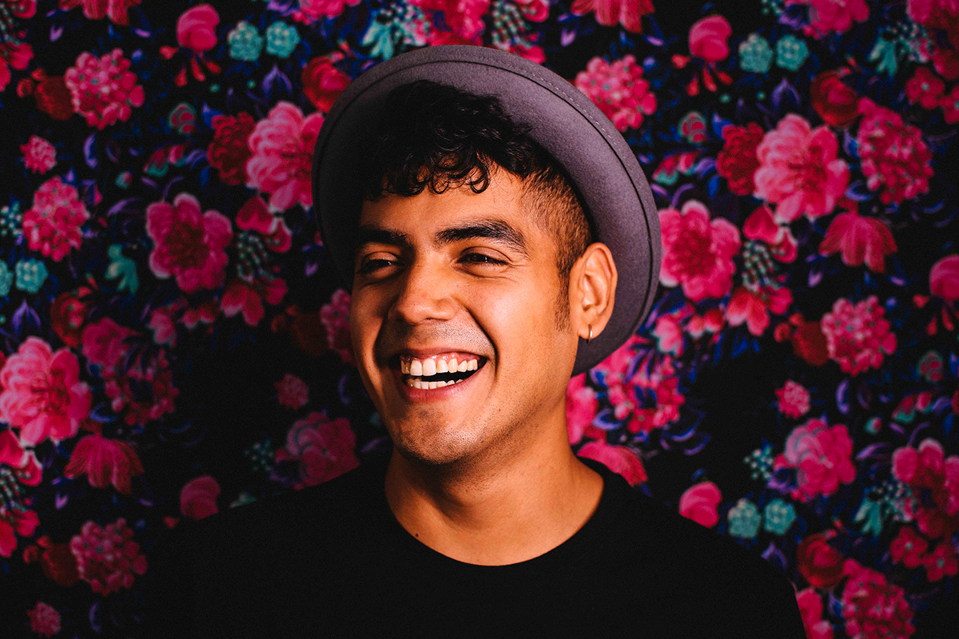 Saul Flores smiling toward the camera while standing in front of a dark floral background
