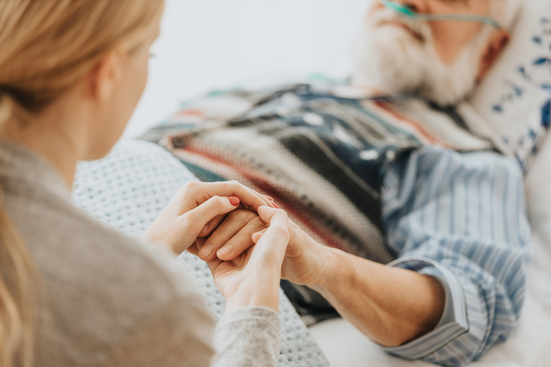 A person holds the hand of an elderly man in a bed.