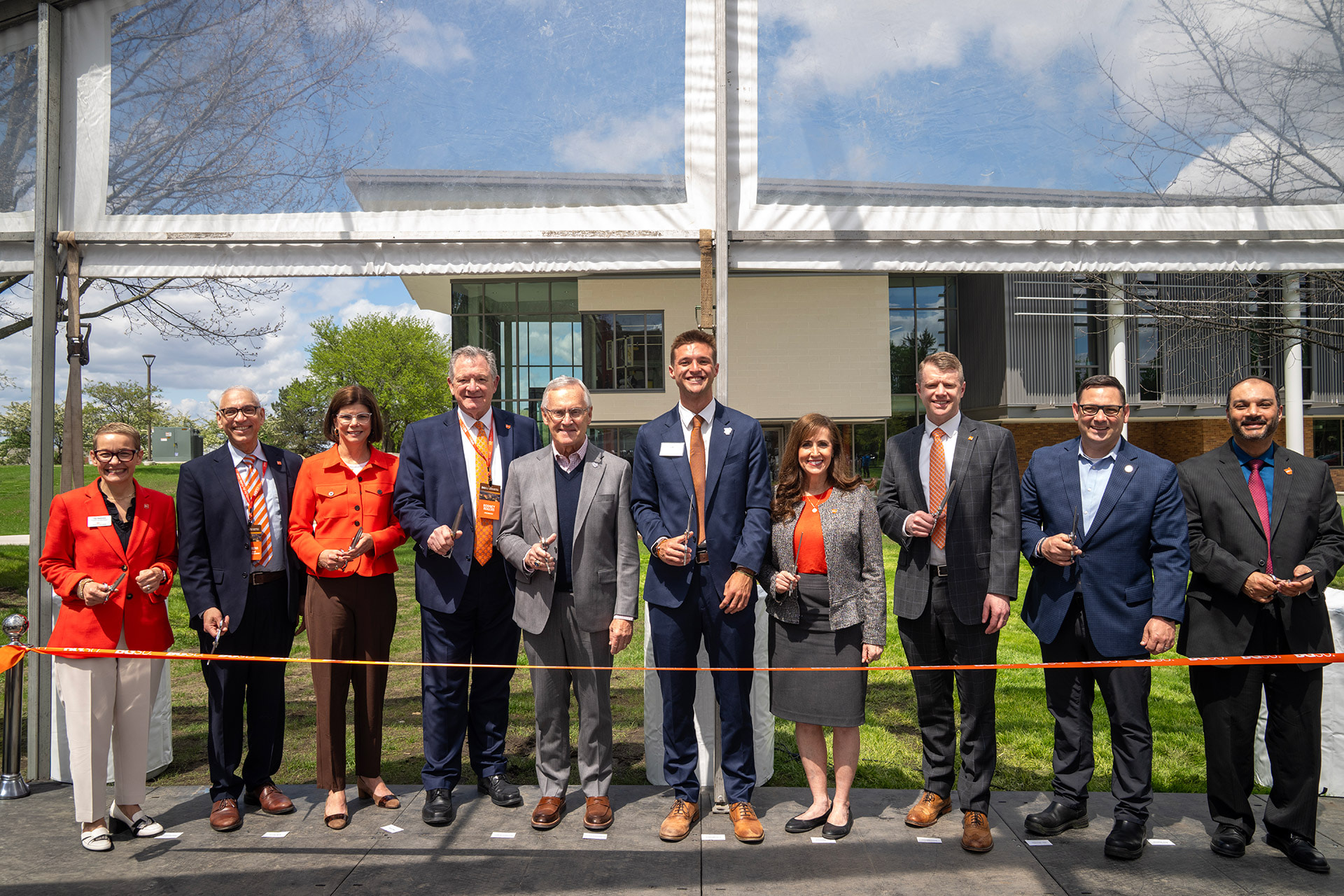 Several people stand behind an orange ribbon during a ribbon-cutting ceremony
