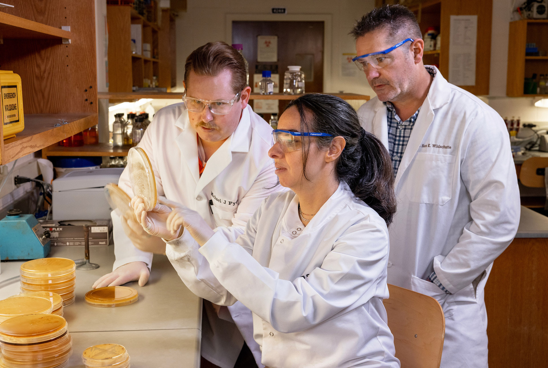 Three scientists examine a petri dish.