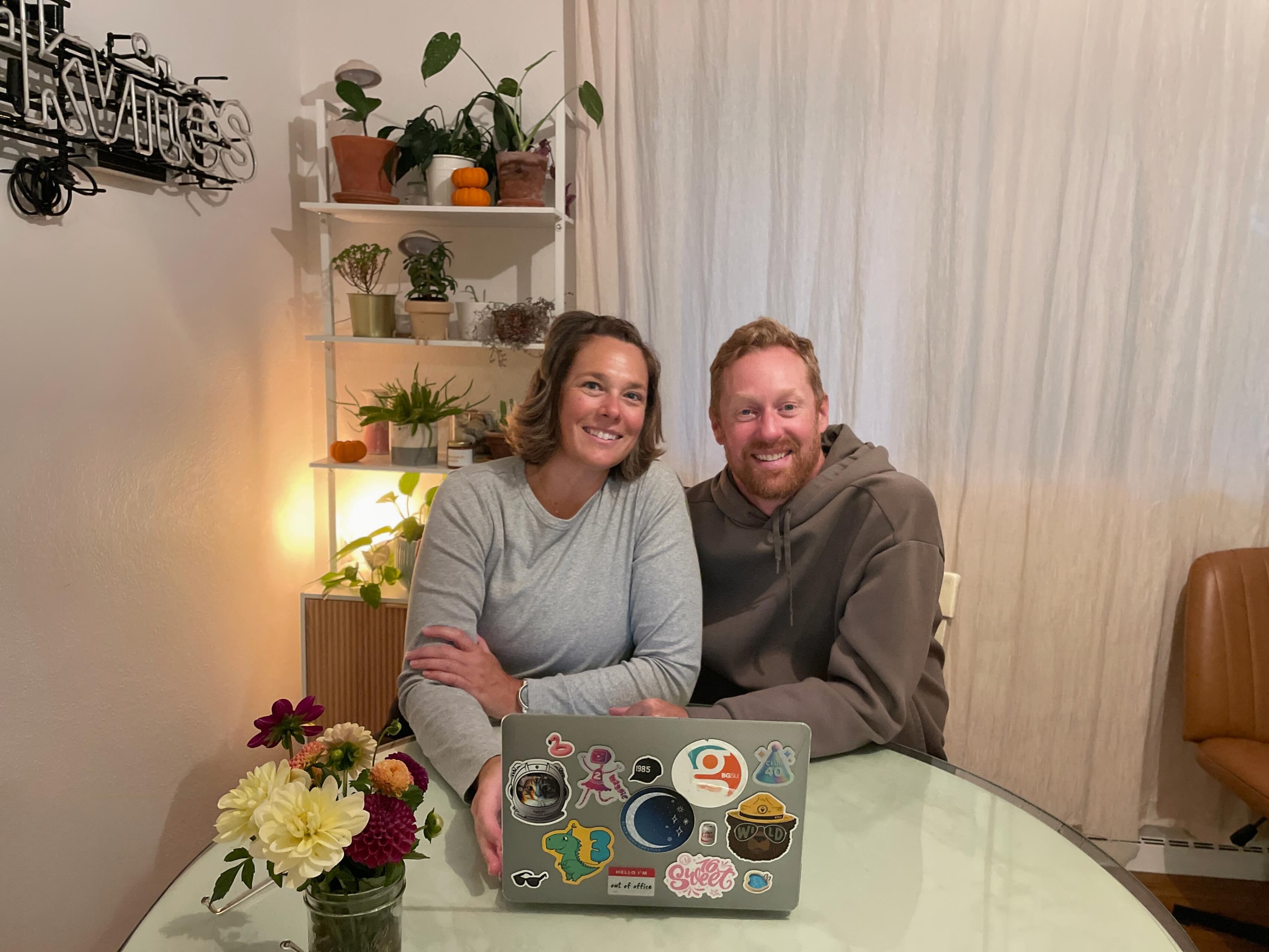 Two people sit at a table with a laptop in front of them